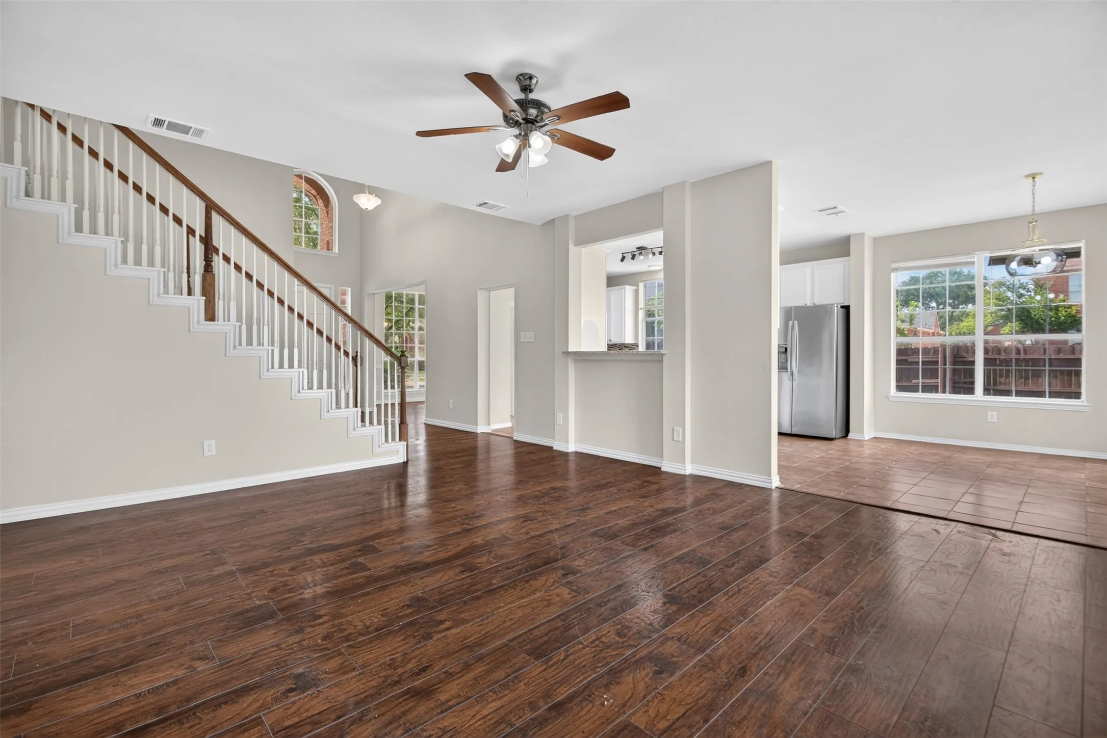 Spacious living area featuring wood-finish flooring, a contemporary ceiling fan, and a prominent staircase with white risers and a dark wood handrail