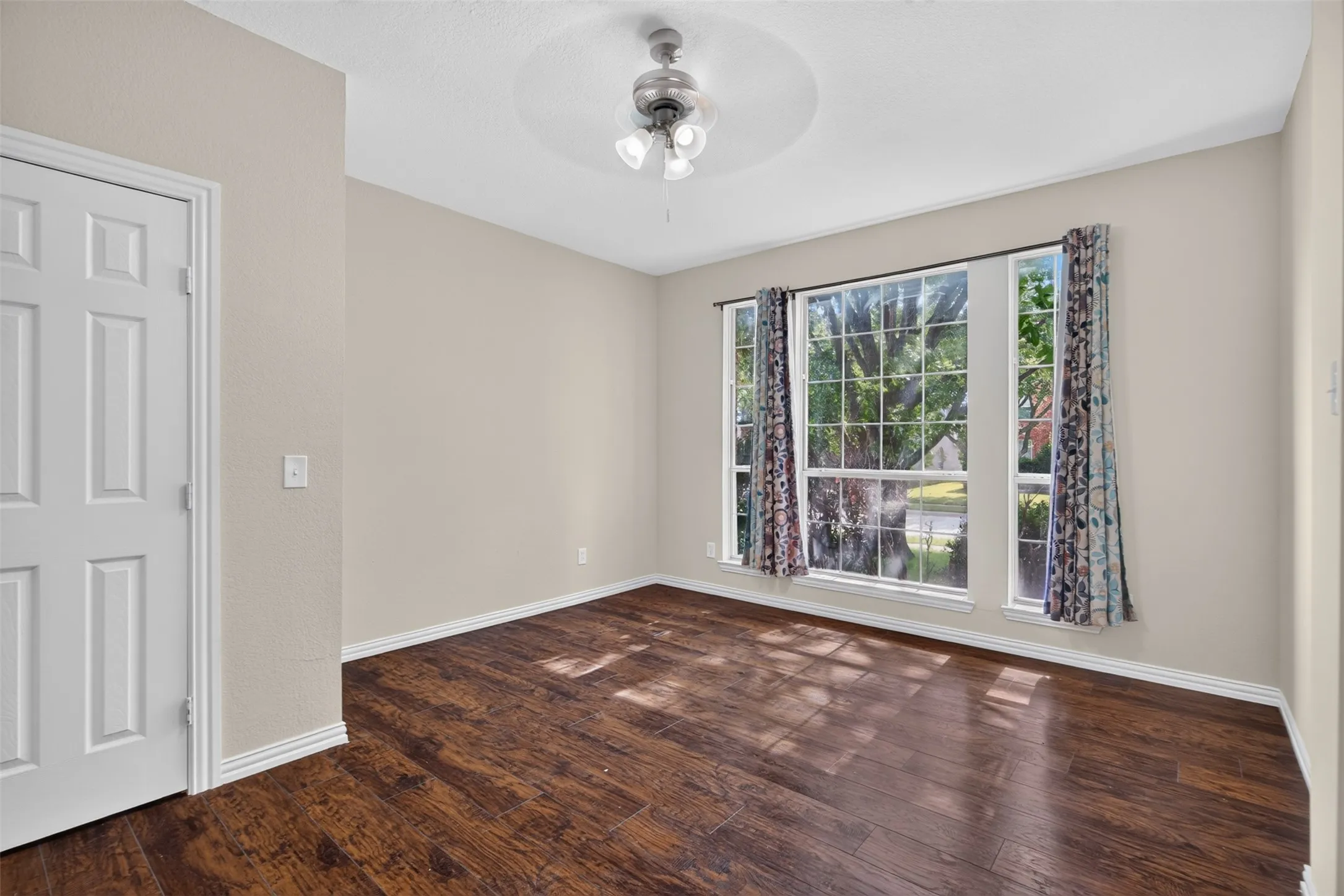 Spacious room featuring rich wood-finish flooring, neutral wall tones, and white baseboards