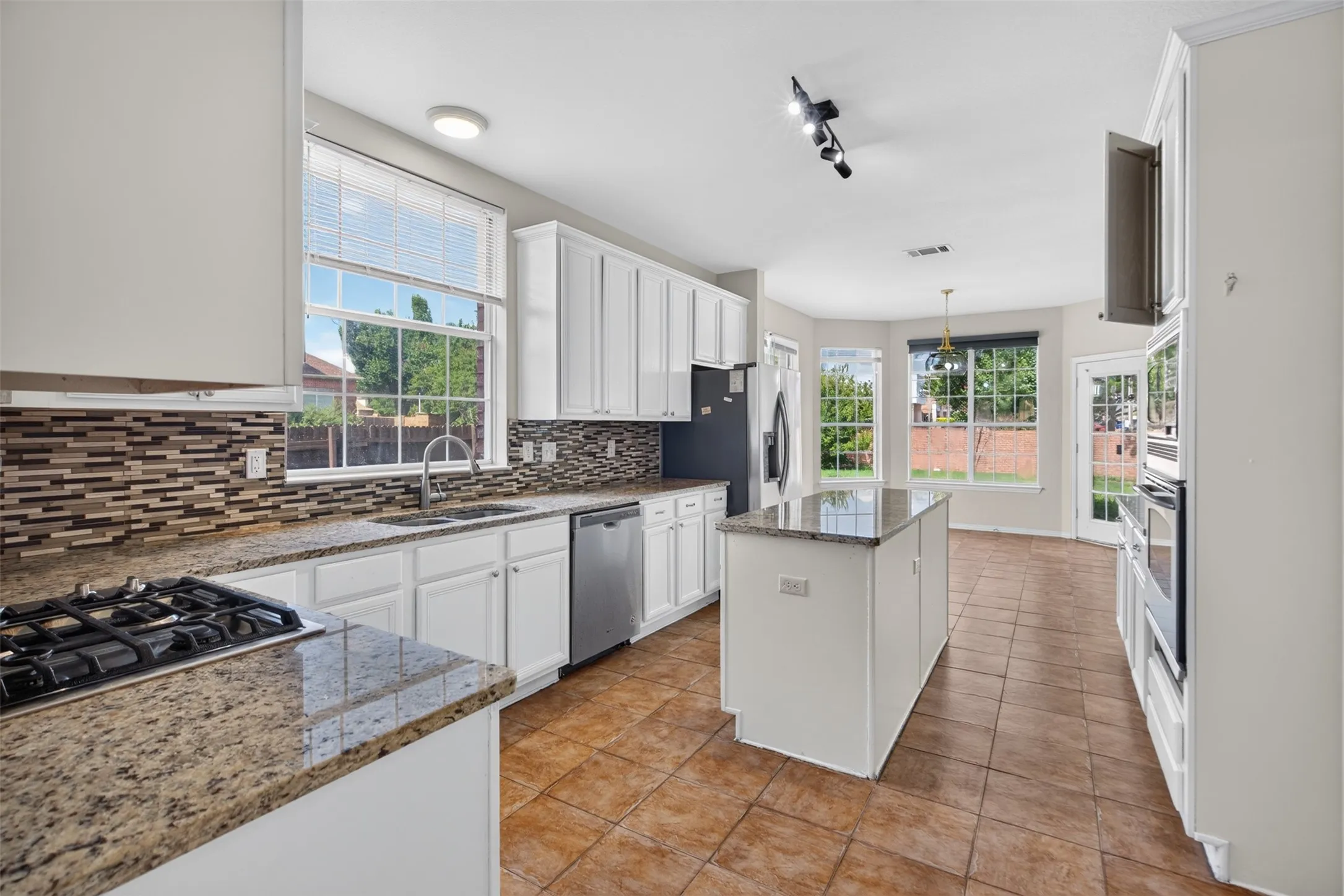 Kitchen featuring white cabinetry, granite countertops, a gas cooktop, a mosaic tile backsplash, and a central island