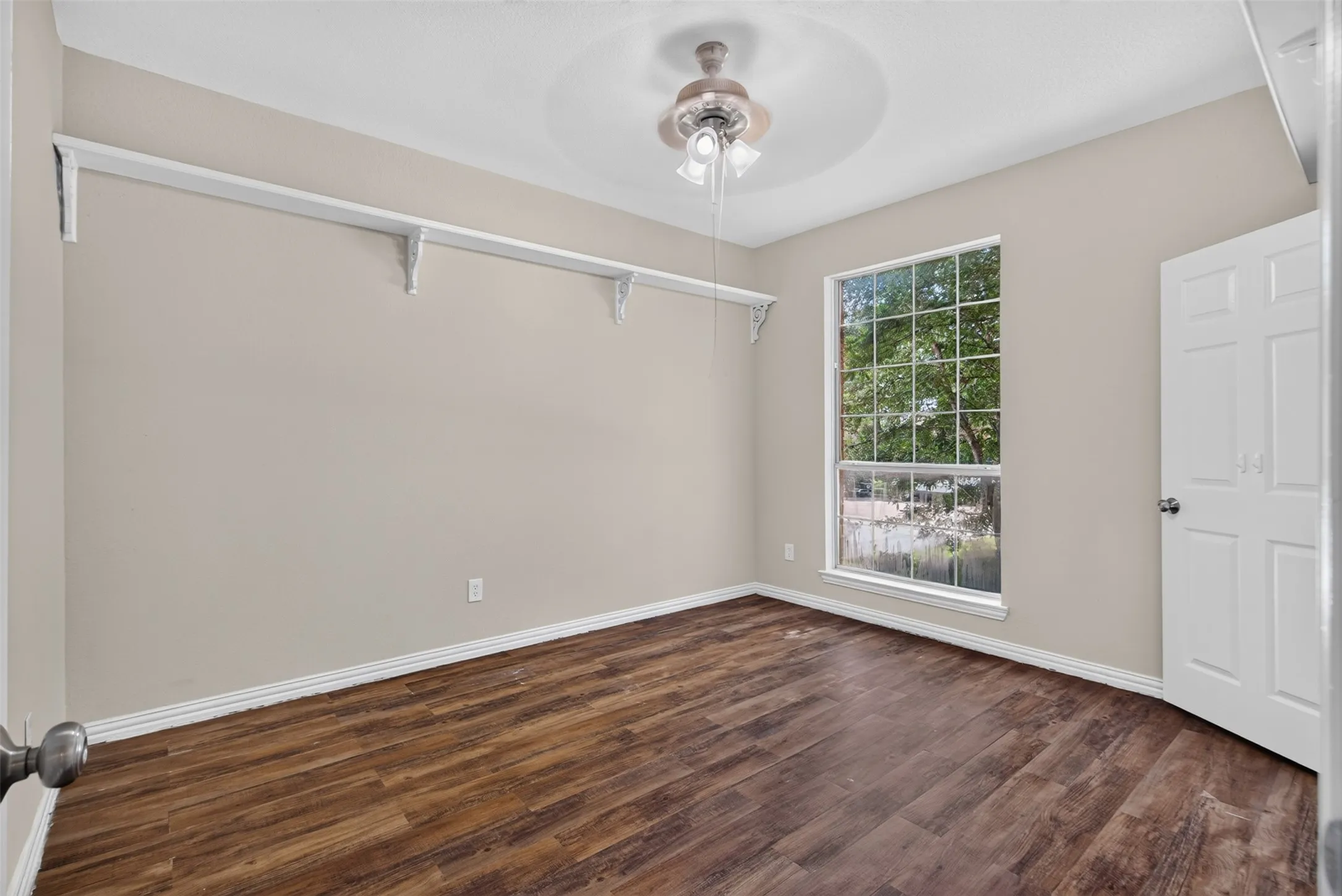 Room featuring wood-finish flooring, a large window, a ceiling fan with light fixture, and a built-in shelving system