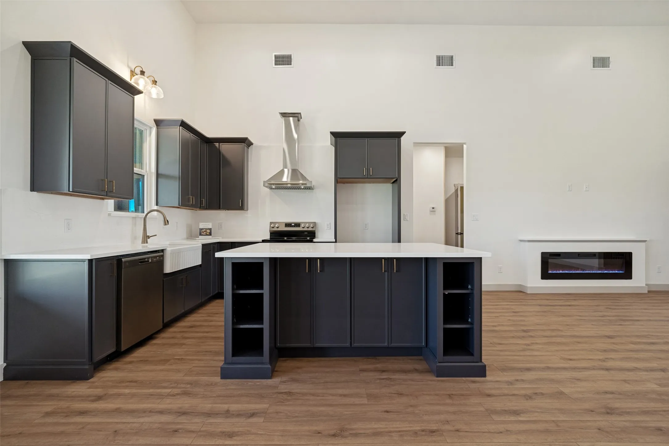 Spacious kitchen featuring dark cabinetry with gold-tone hardware, white countertops, a large center island with integrated shelving, and stainless steel appliances