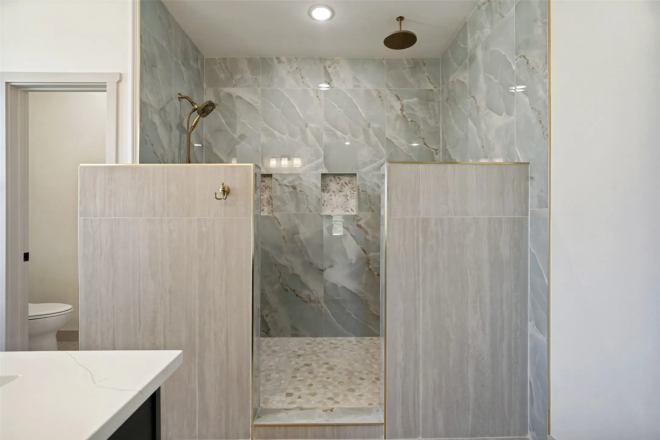 Walk-in shower featuring jaw stopping marbled tile walls, a pebbled floor, and dual shower heads.