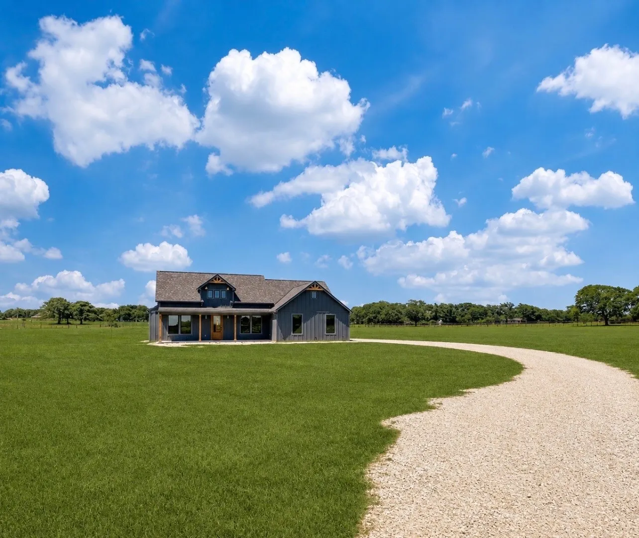Gray siding exterior with gable rooflines, covered porch, exposed wood columns, and a gravel driveway