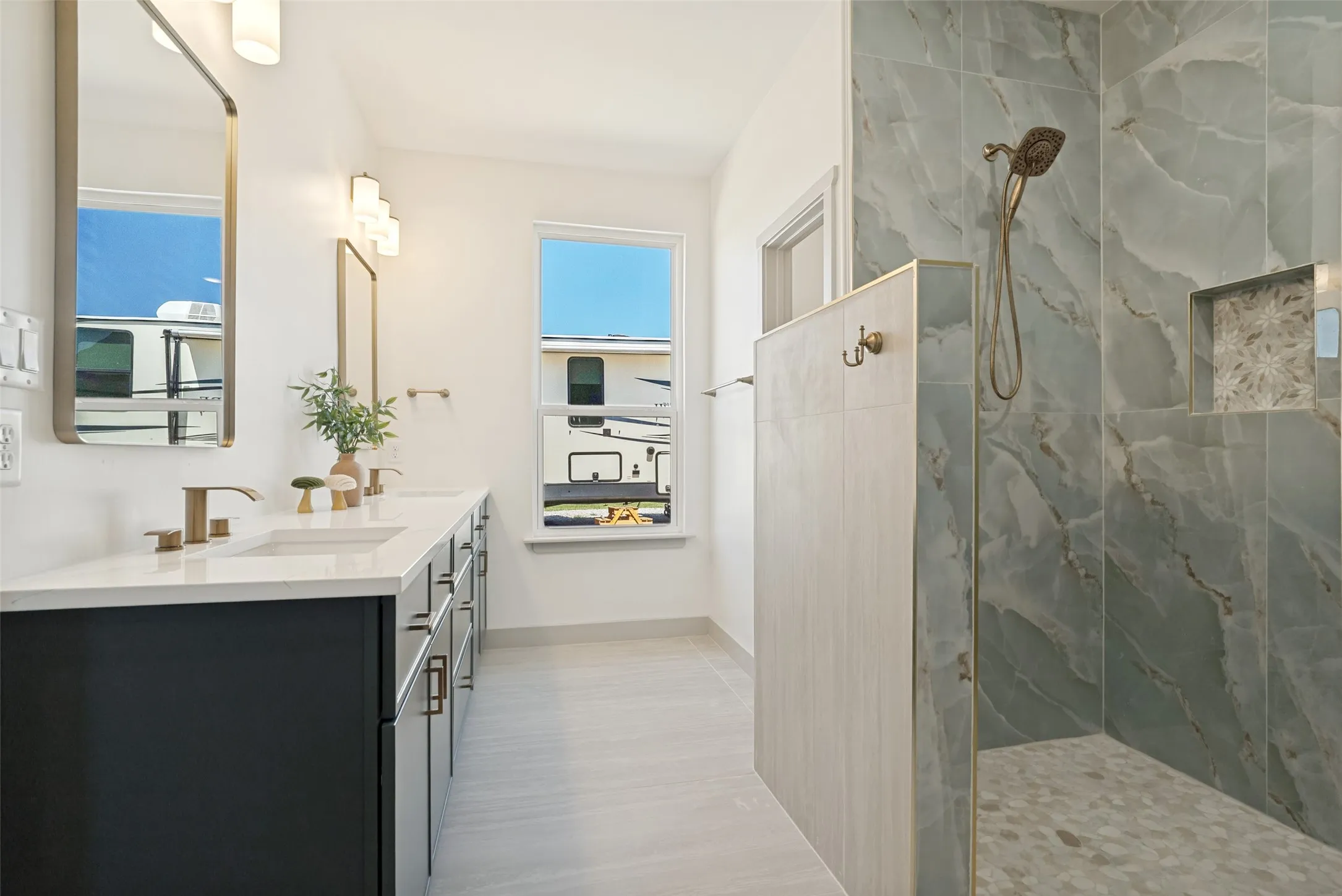 Modern en-suite bathroom in primary bedroom featuring a double vanity with dark cabinetry and white countertops and a gorgeous spa-like shower area.