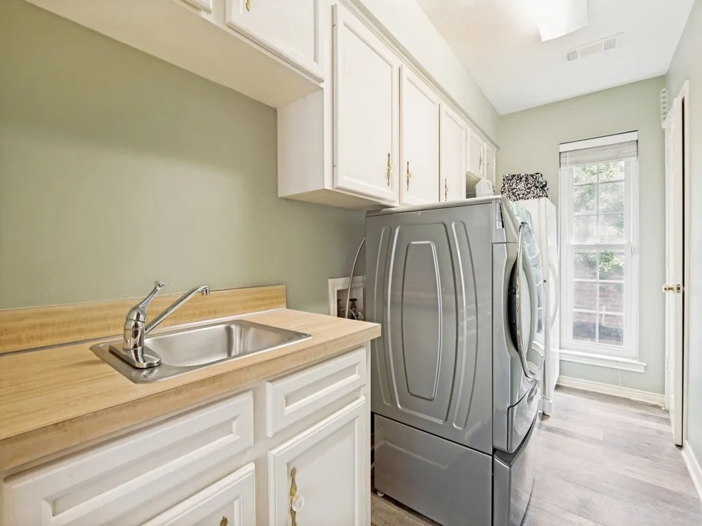 Dedicated laundry room featuring white cabinetry, a utility sink with a wood-finish countertop, and wood-finish flooring