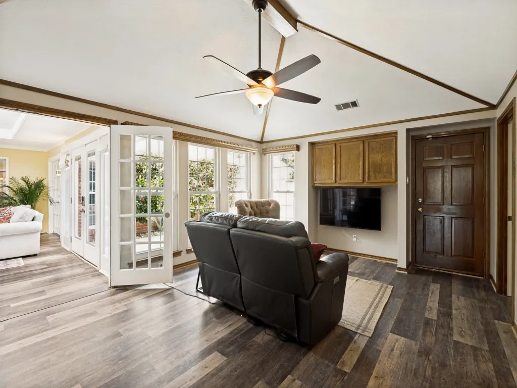 Living area featuring wood-finish flooring, vaulted ceiling with a ceiling fan, and built-in cabinetry above a television mount