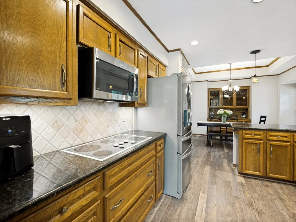 Kitchen featuring wood cabinetry with metal hardware, dark countertops, a built-in cooktop, and a tile backsplash
