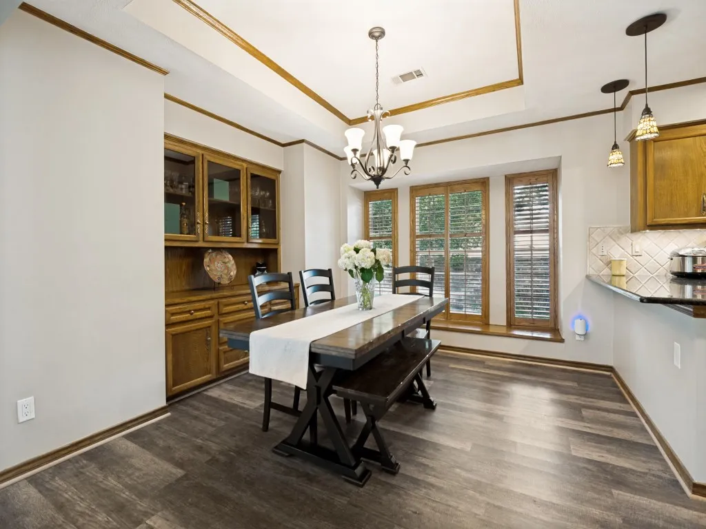 Dining area featuring wood-finish flooring, a built-in wood hutch with glass-front cabinetry, multiple windows with wood blinds, and a tray ceiling with crown molding