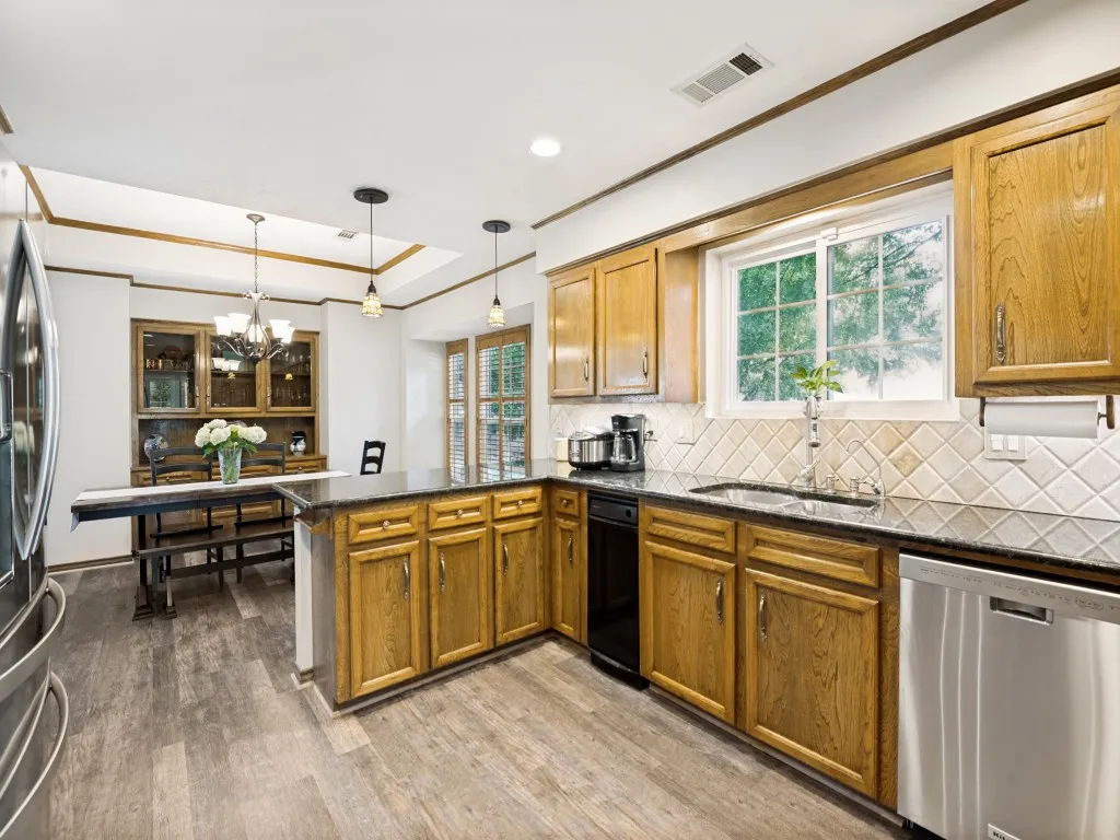 Open kitchen with wood-finish flooring and L-shaped granite countertops