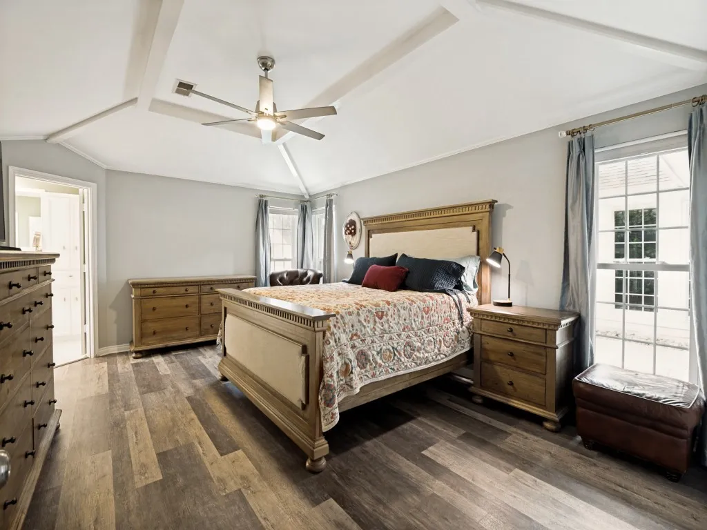 Spacious room featuring vaulted ceilings with decorative beams, wood-finish flooring, and a ceiling fan