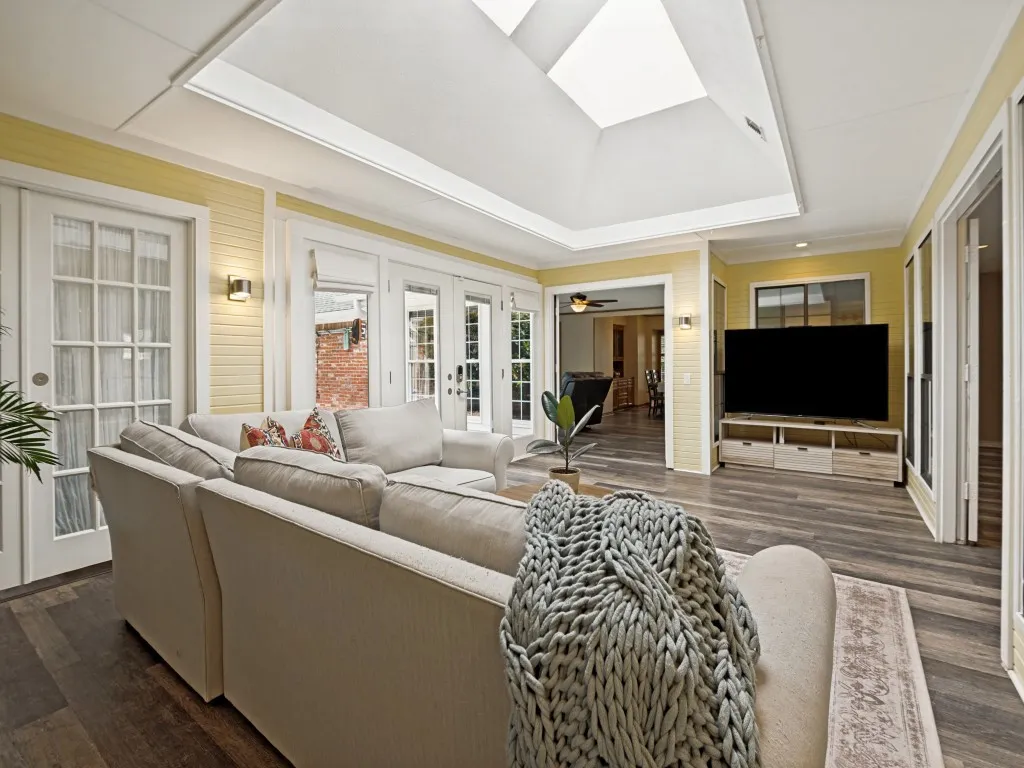 Expansive living area featuring a vaulted ceiling with skylights, wood-finish flooring, and multiple glass-paneled doors