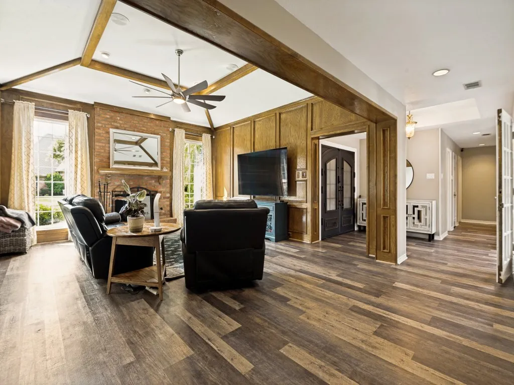 Spacious living area featuring wood-finish flooring, exposed wood beams, and a brick fireplace