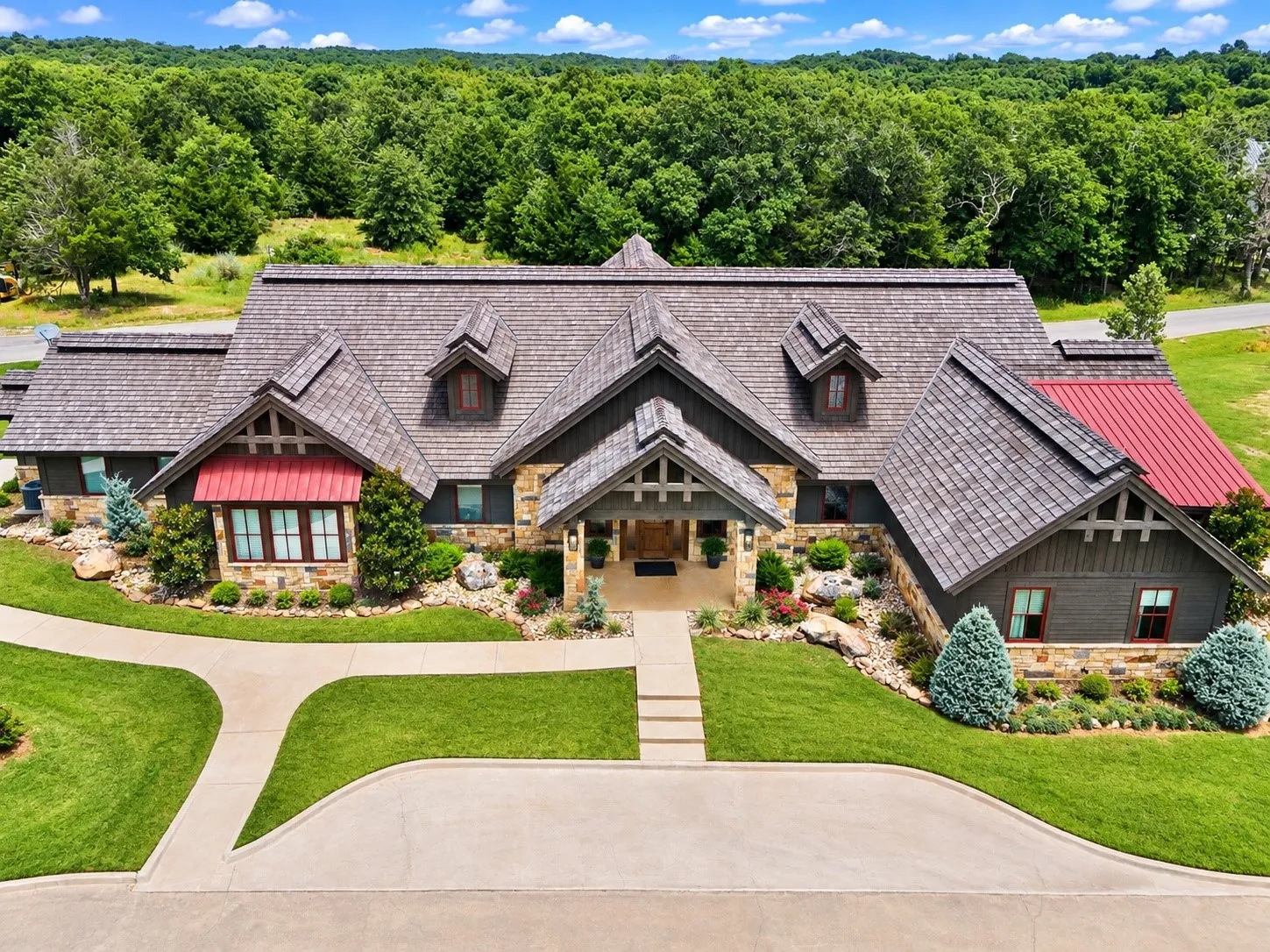 Multi-gabled property featuring a natural stone facade, cedar shake roofing, and a red metal awning accent