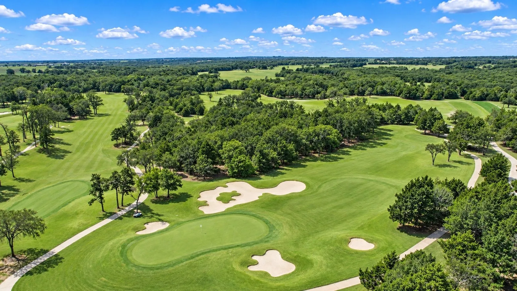 Expansive golf course setting featuring manicured green fairways, sand bunkers, and mature trees