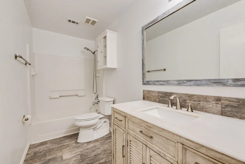 Bathroom featuring wood-finish flooring, a white vanity with an integrated sink, brushed nickel faucet, and a large framed mirror
