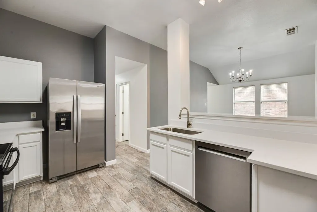 Kitchen featuring stainless steel appliances, white cabinetry, light countertops, a stainless steel sink with a gooseneck faucet, and wood-finish flooring