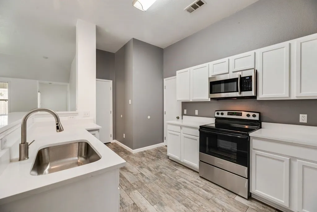 Kitchen featuring white cabinetry, light-toned countertops, a stainless steel sink with a gooseneck faucet, a stainless steel microwave, and a black and stainless steel range