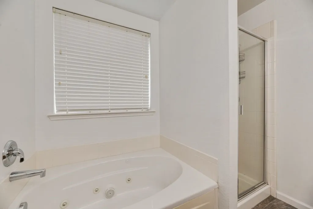 Built-in jetted tub with chrome fixtures, a privacy blind-equipped window, and an enclosed shower with glass door