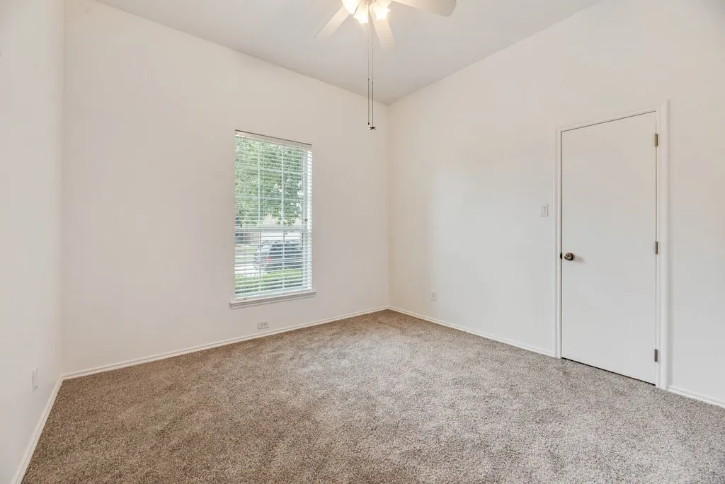Spacious room featuring vaulted ceilings, light-colored walls, carpet flooring, a window with blinds, and a ceiling fan