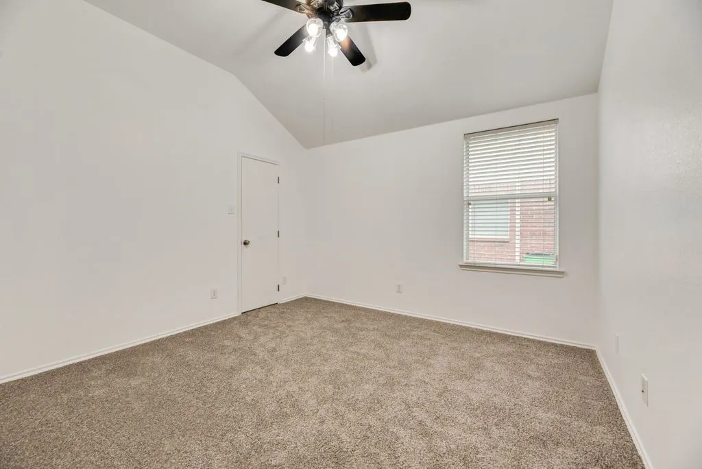 Vaulted ceiling room featuring neutral-toned carpet, a window with blinds, and a ceiling fan with integrated lighting