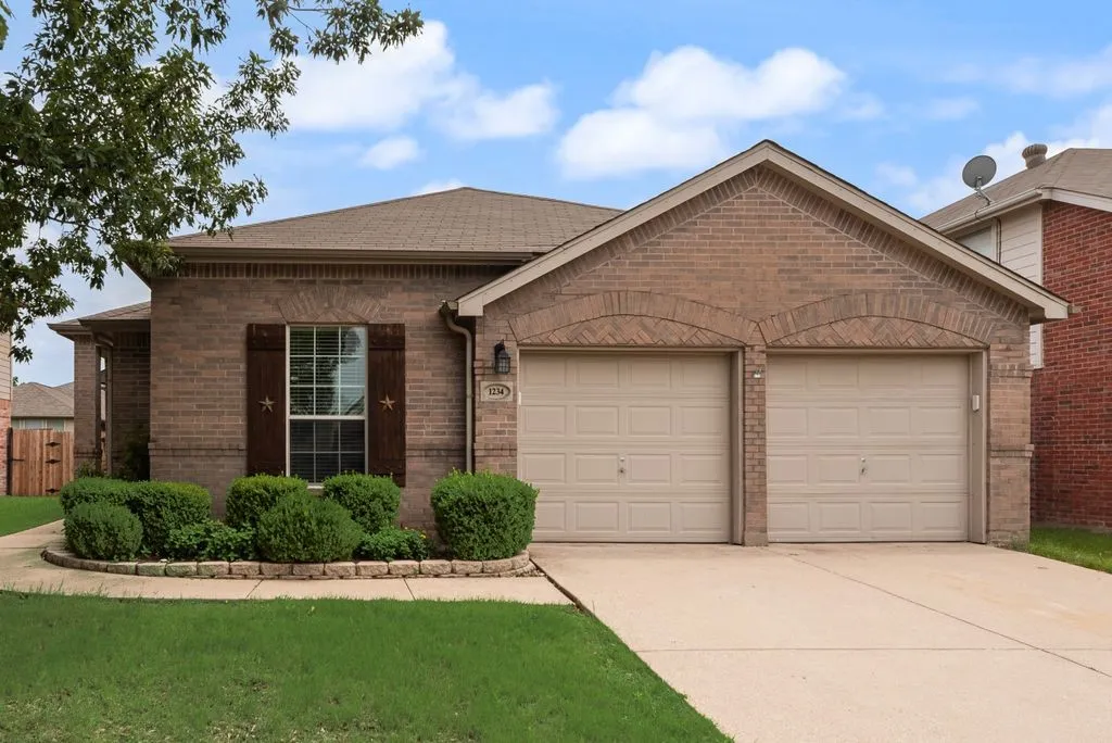 Brick facade home with a two-car garage, arch detailing over garage doors, wood-finish window shutters, and a concrete driveway