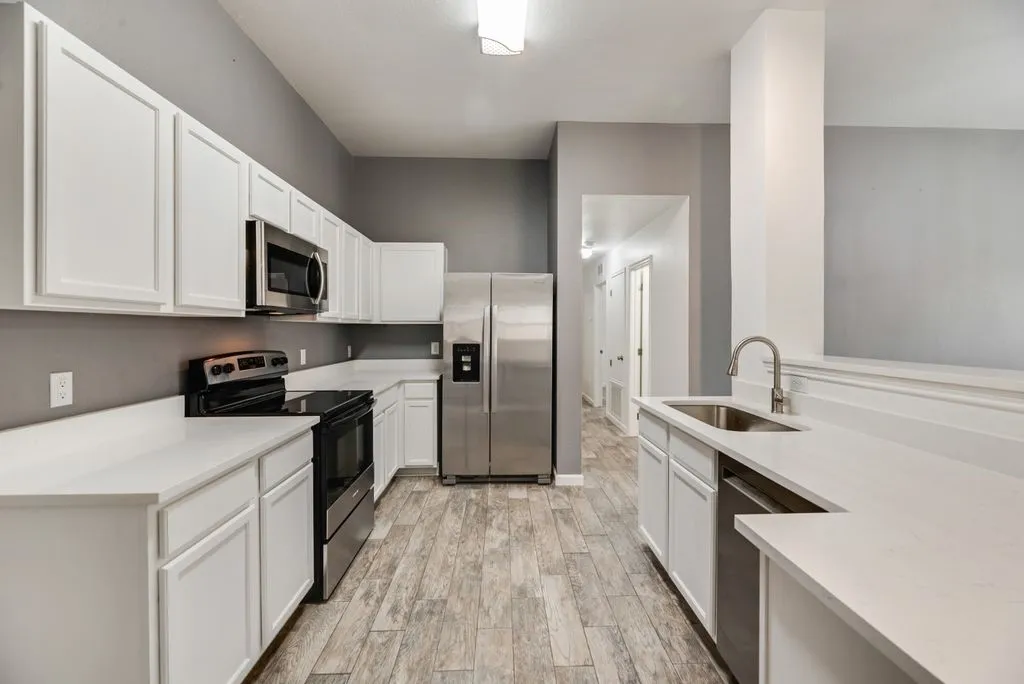 Kitchen featuring white shaker-style cabinetry, stainless steel appliances, light-toned countertops, and wood-finish flooring