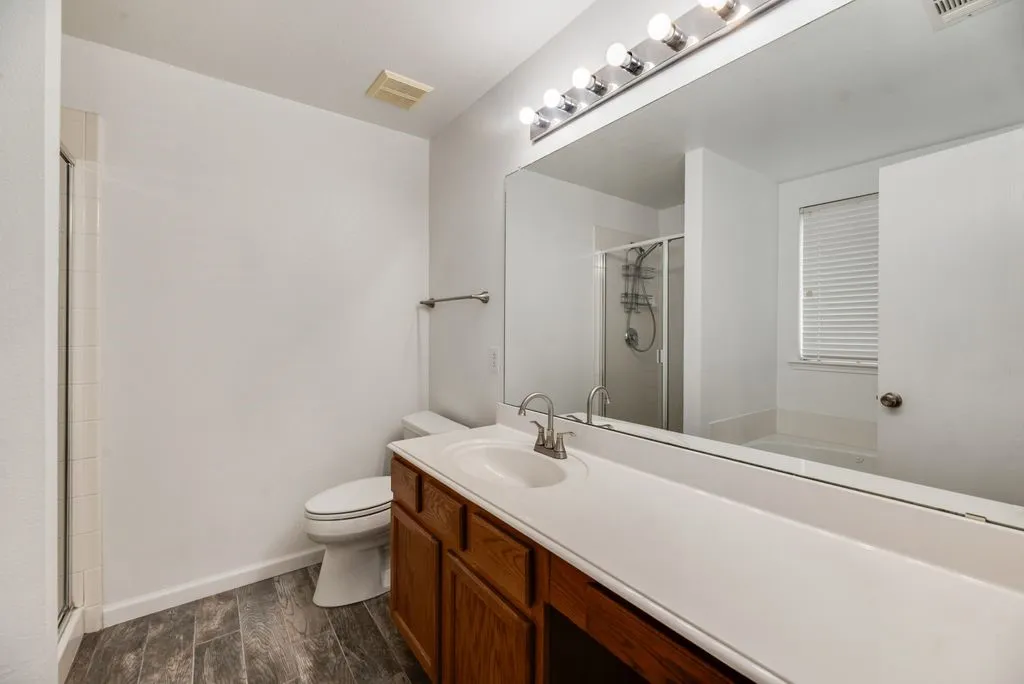 Bathroom featuring a spacious vanity with dual sinks, wood-finish cabinetry, and a large mirror with integrated lighting