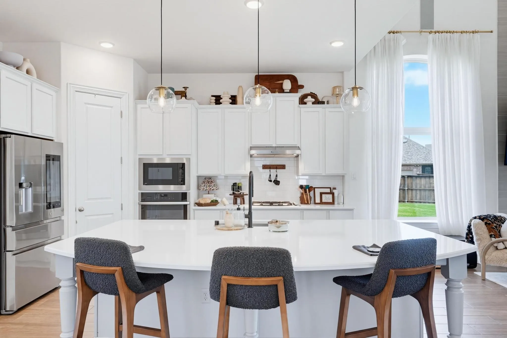 Expansive kitchen featuring a large central island, white cabinetry, stainless steel appliances, and wood-finish flooring
