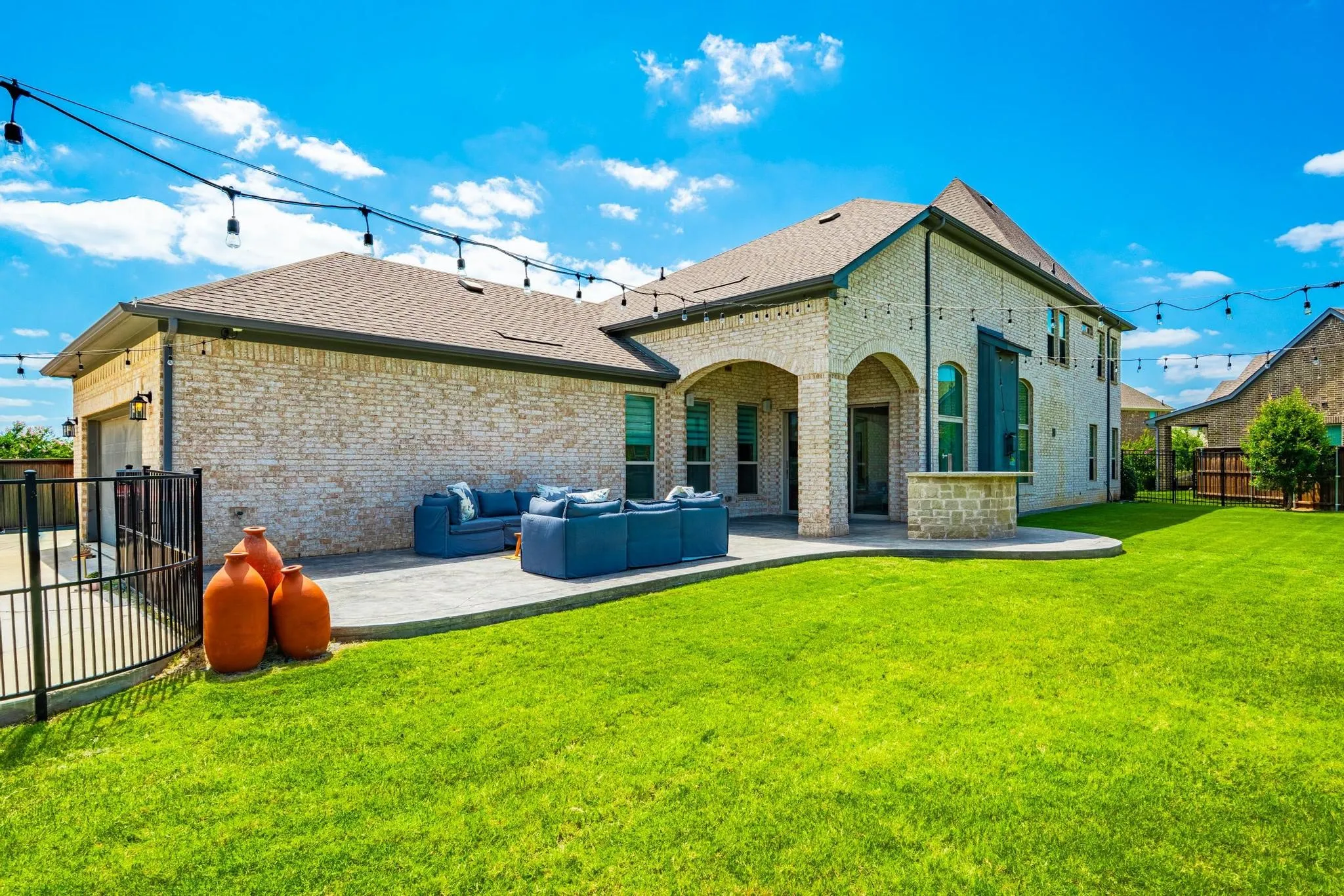 Expansive backyard featuring a manicured lawn, string lighting, and a brick exterior