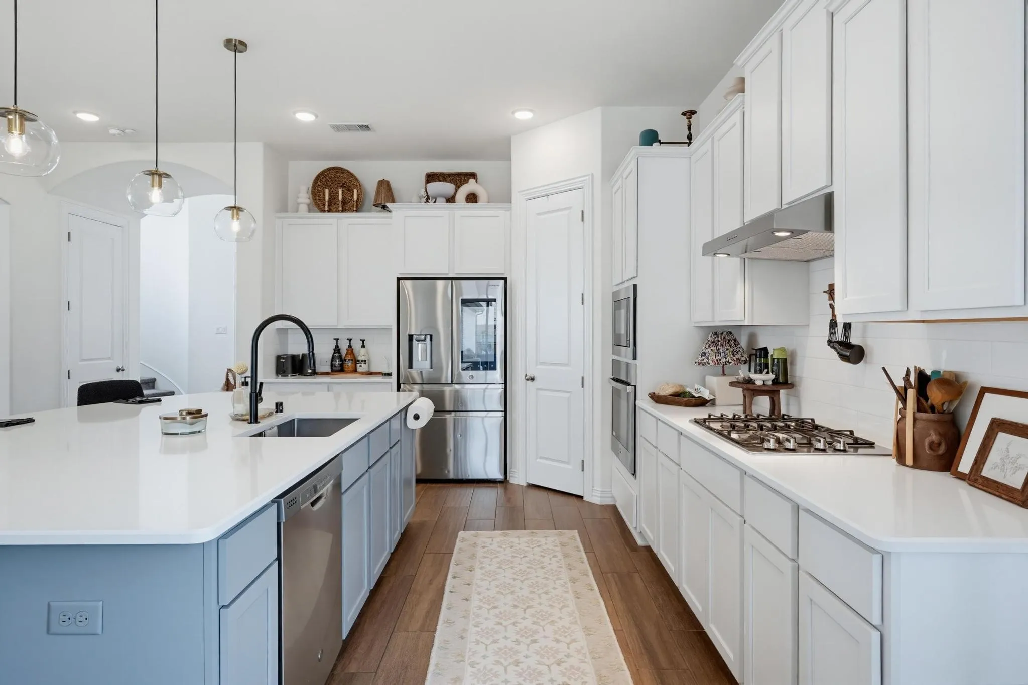 Kitchen featuring a large central island with a built-in sink and dishwasher, white countertops, wood-finish flooring, white cabinetry, and stainless steel appliances