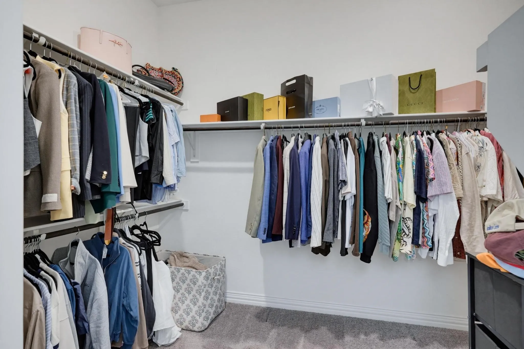 Walk-in closet featuring extensive built-in shelving, multiple hanging rods, white walls, gray carpet flooring, and white baseboards