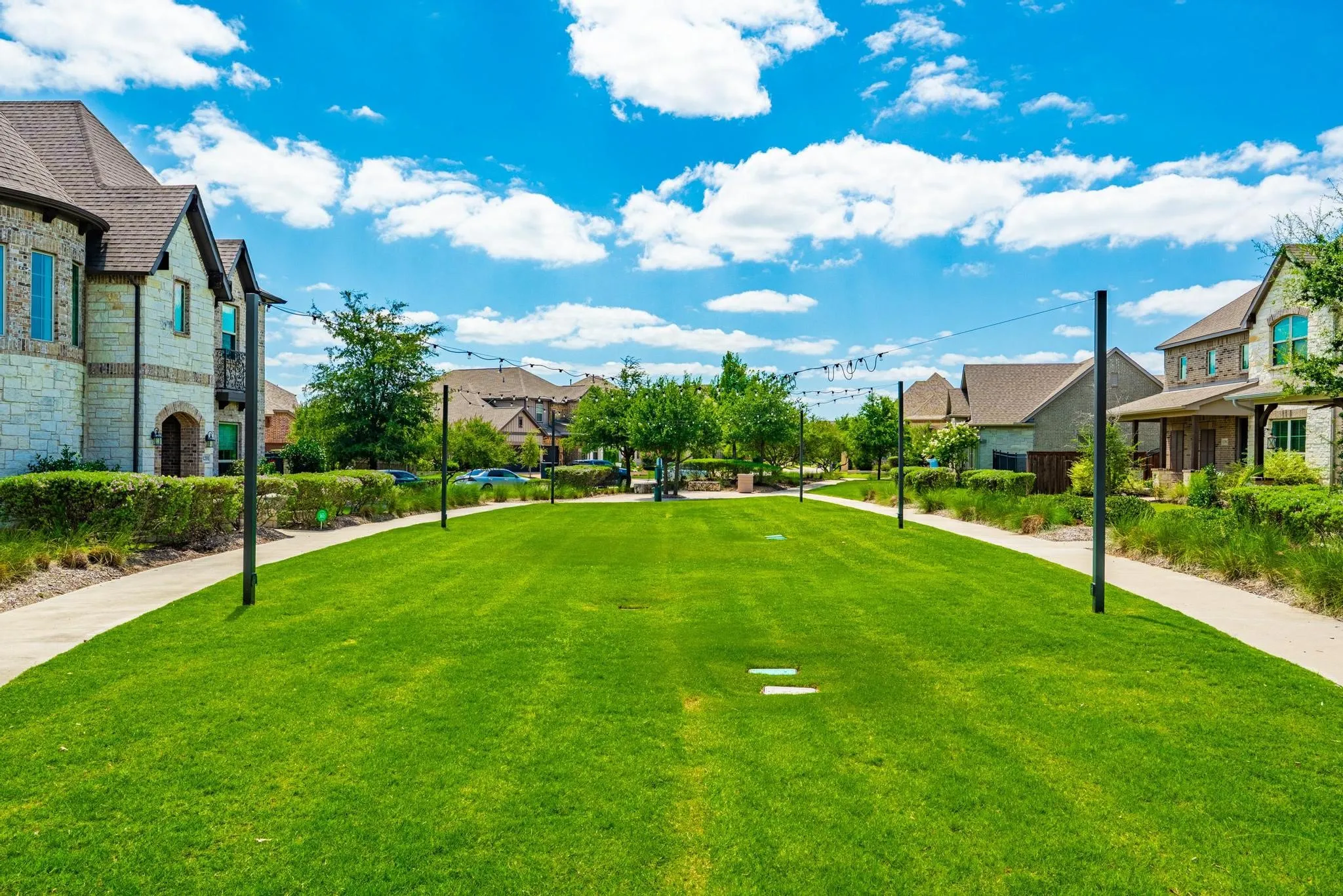 Expansive green space featuring a manicured lawn, paved pathways, and decorative string lighting