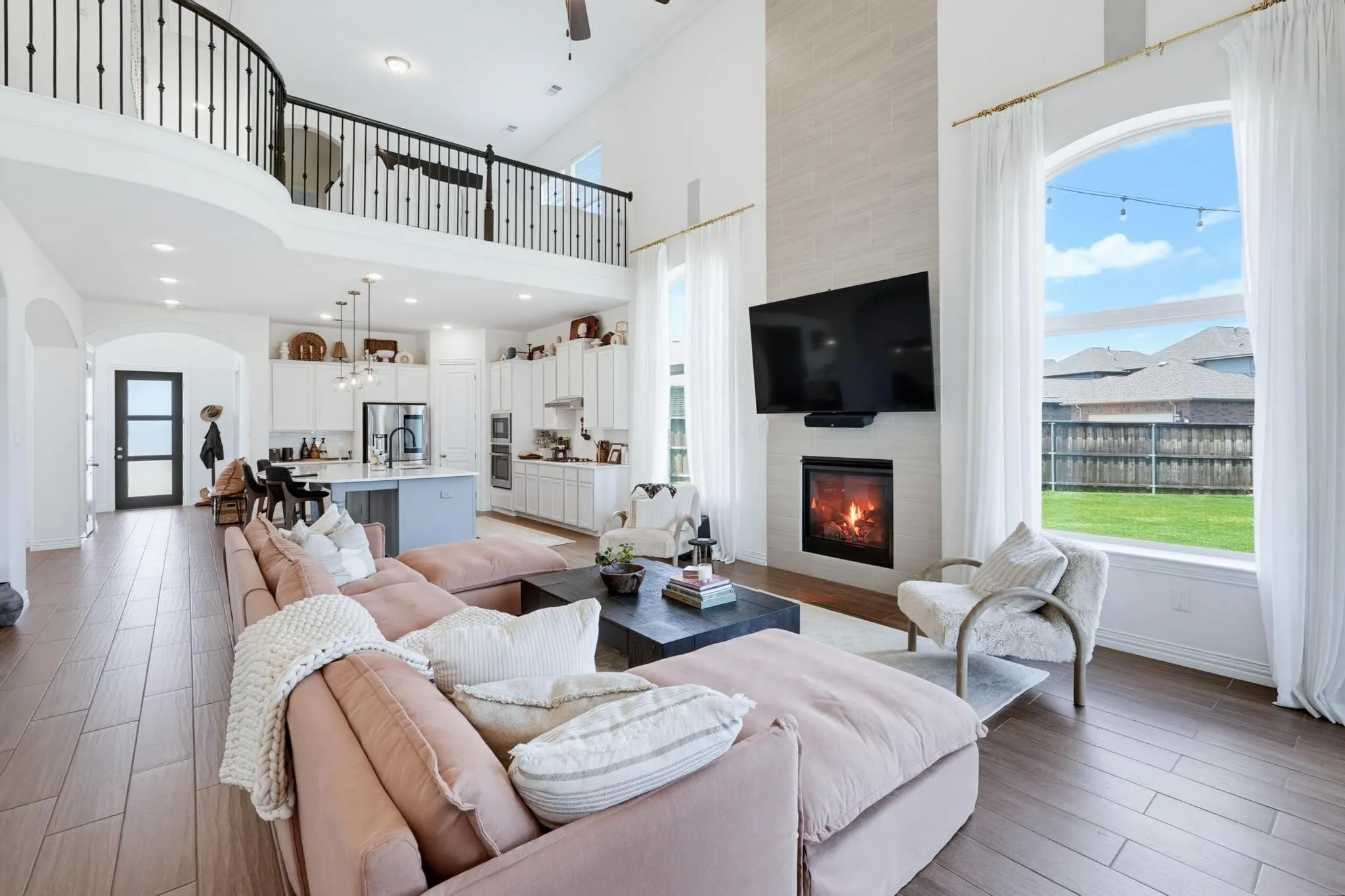 Open-concept living space featuring wood-finish flooring, a two-story ceiling, and a fireplace with a light-toned tile surround