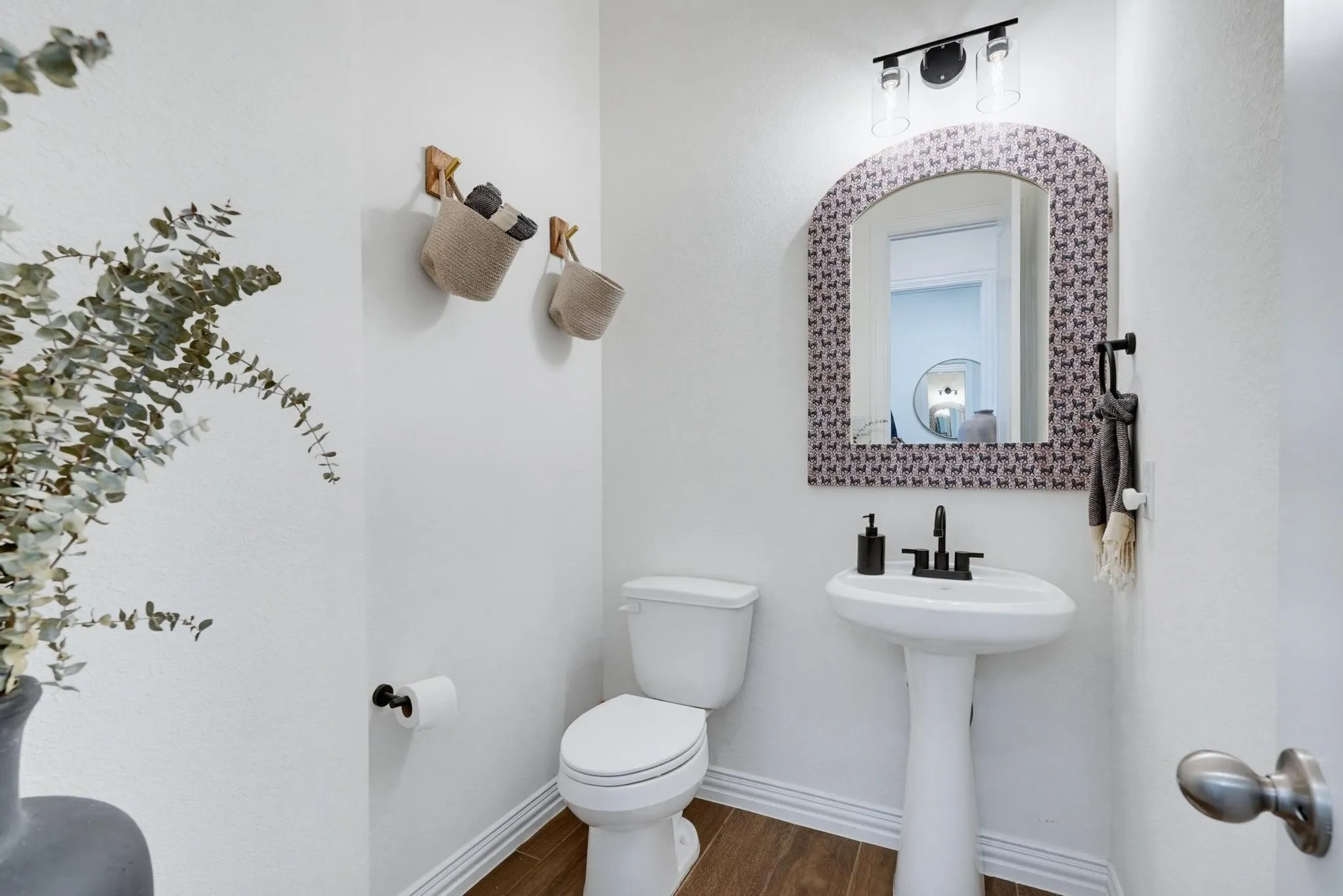 Powder room featuring a pedestal sink, black-finish faucet, and wood-finish flooring