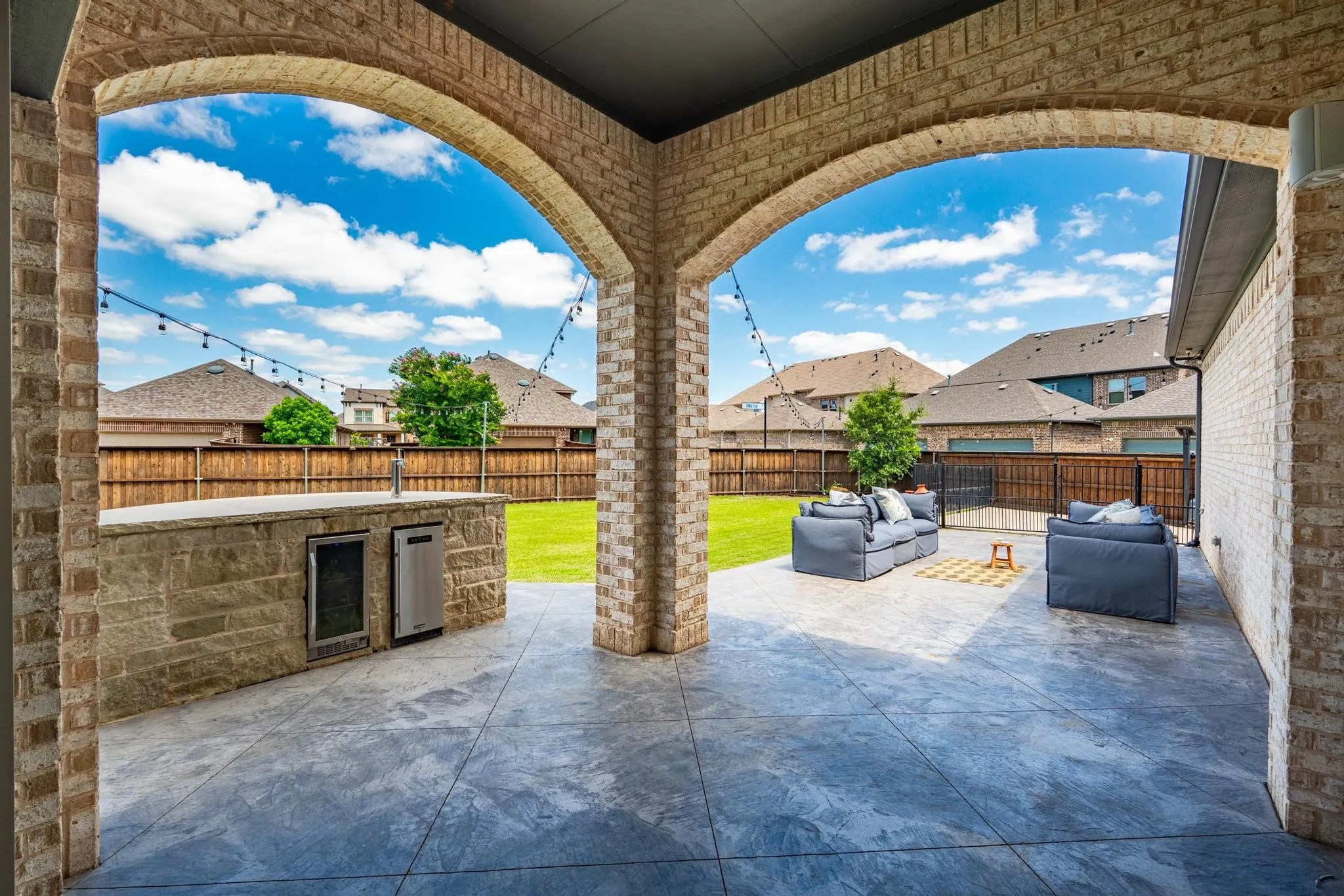 Covered patio with brick arches and a stone-clad outdoor kitchen featuring built-in appliances