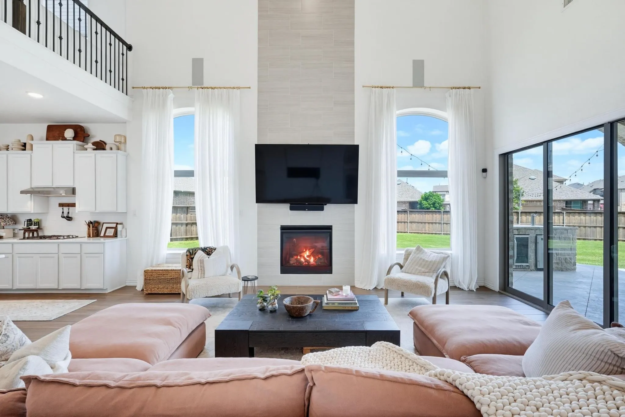 Two-story great room featuring a contemporary fireplace with a tile surround, wood-finish flooring, and a second-story balcony with metal balusters
