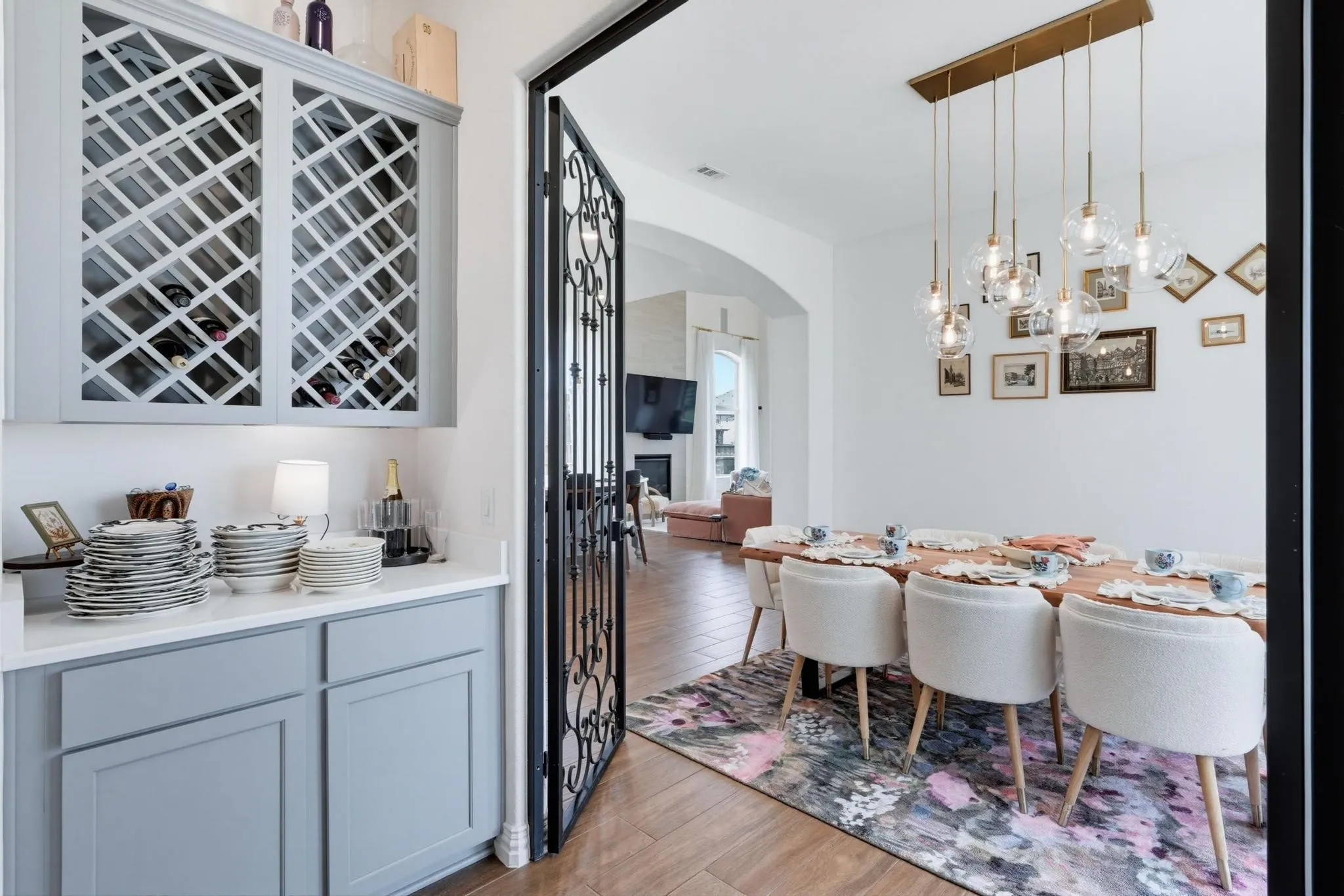 Formal dining area featuring a linear chandelier with multiple glass globe pendants, wood-finish flooring, a white accent wall, and an ornate wrought-iron door