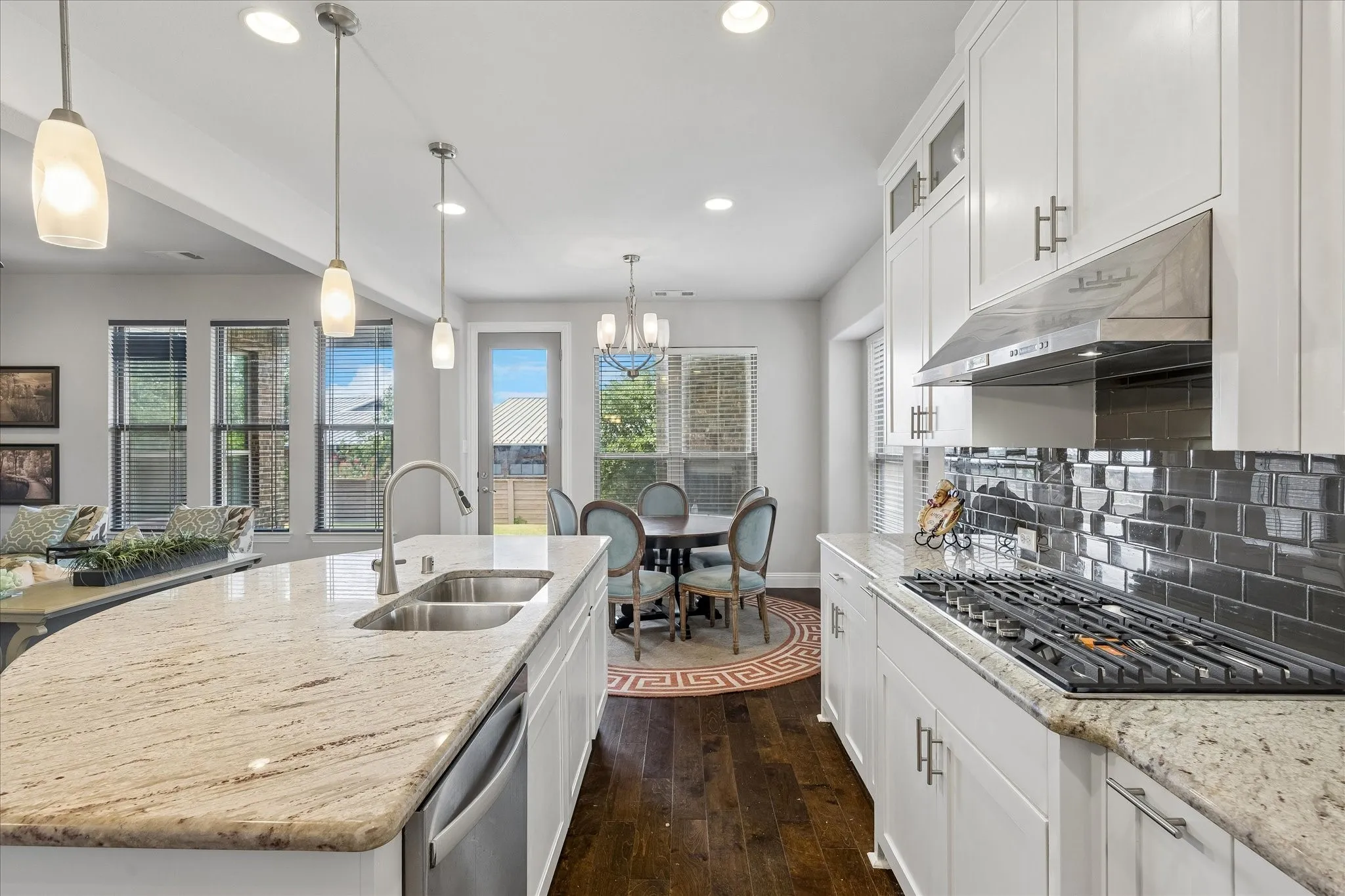 Kitchen featuring an oversized island with double basin stainless steel sink, granite countertops, stainless steel appliances, white cabinetry, and dark subway tile backsplash
