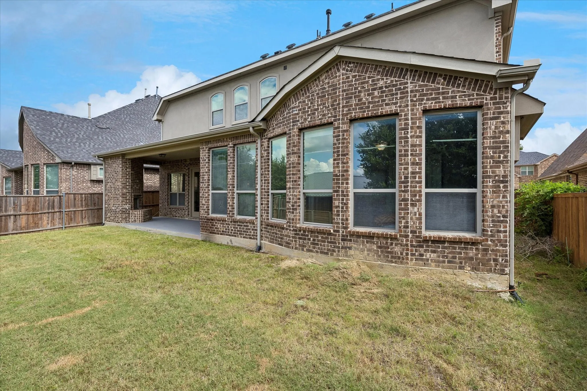 Expansive backyard featuring a concrete patio, brick exterior, multiple large windows, and a wood privacy fence