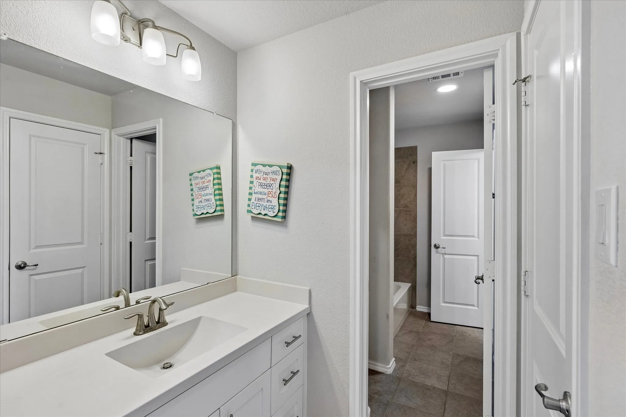 Bathroom vanity featuring a single sink, brushed nickel faucet, large mirror, and three-light fixture