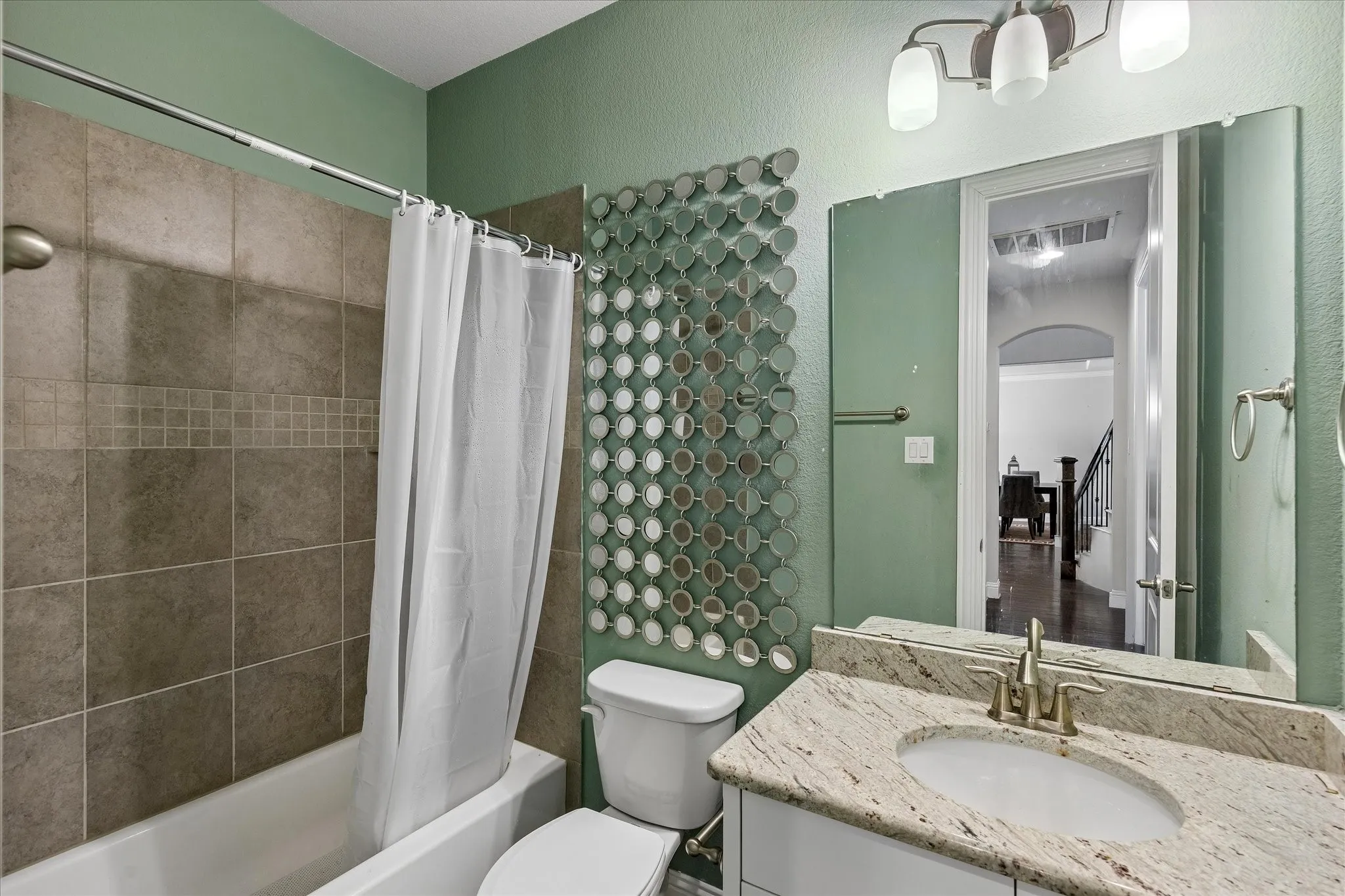 Bathroom featuring a tub/shower combination with tile surround, a single vanity with stone countertop, and a circular mirror accent wall