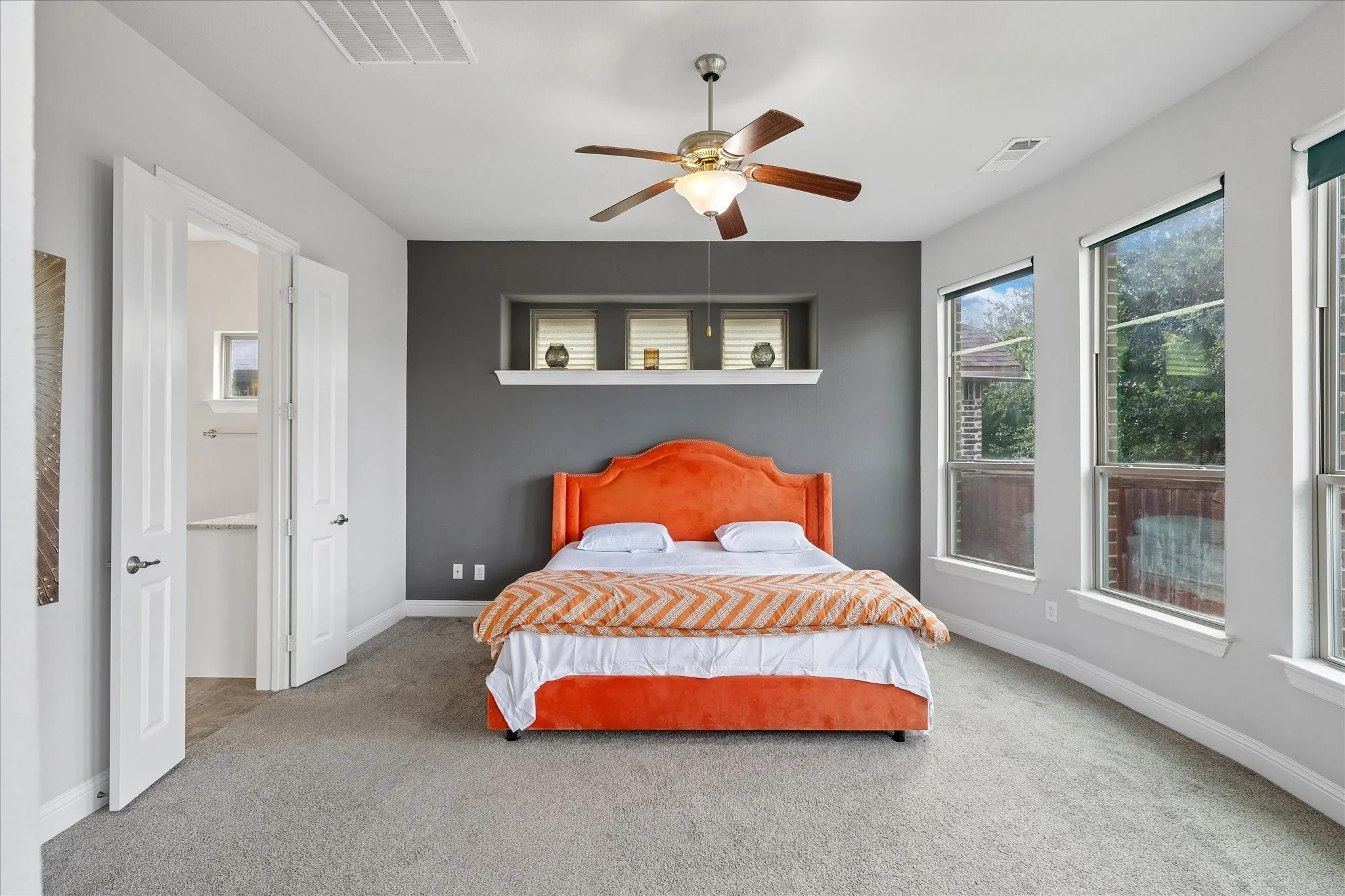 Carpeted bedroom featuring multiple windows, a ceiling fan, a contrasting accent wall, and double doors opening to an adjoining room