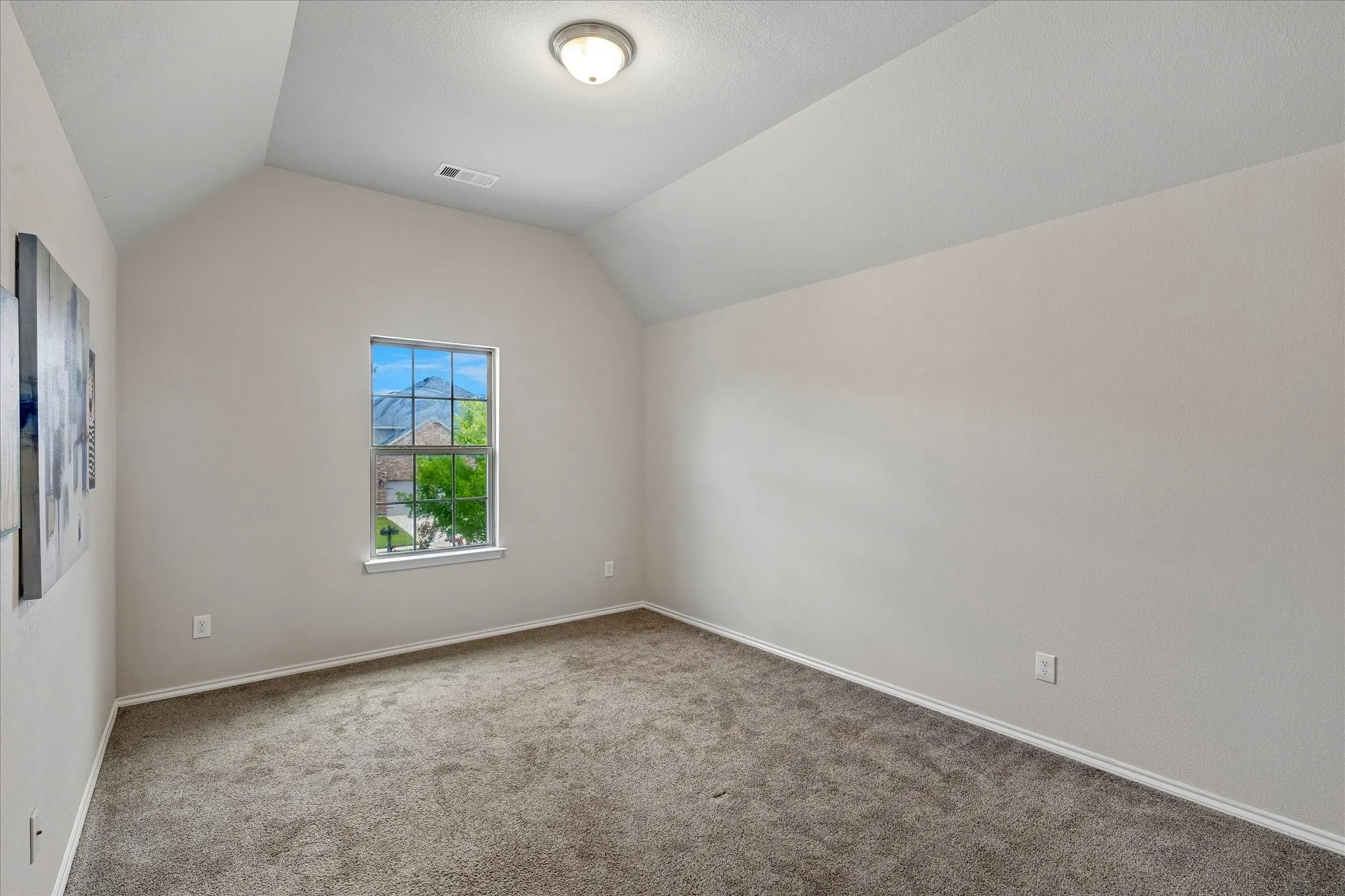 Vaulted ceiling room with neutral-toned carpet flooring and a single pane window providing natural light