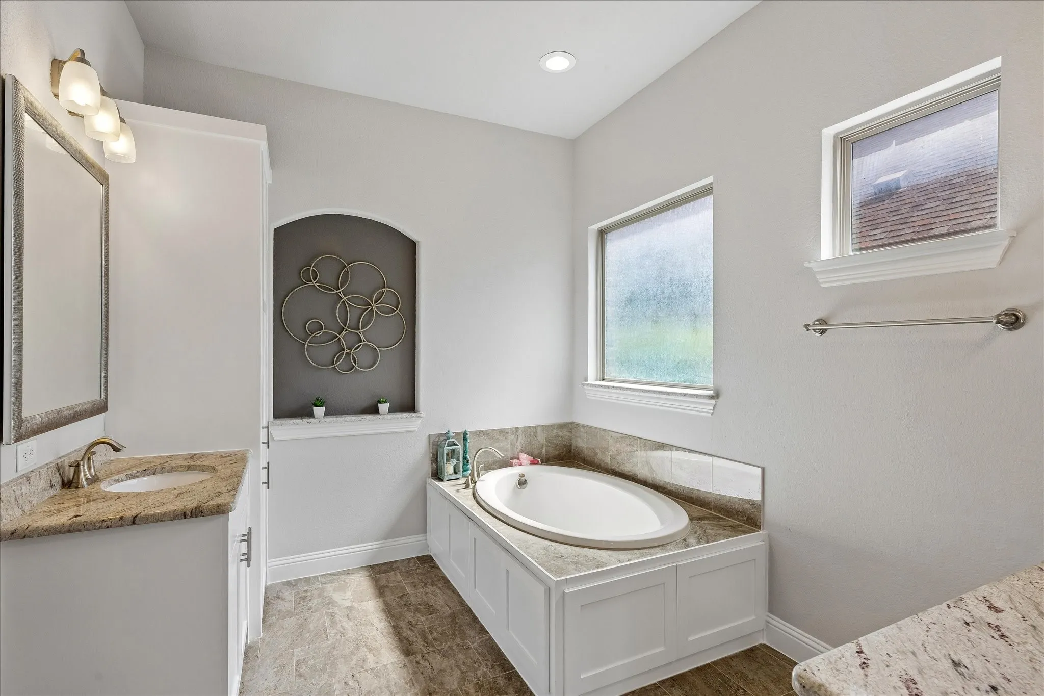 Soaking tub with surrounding stone-finish tile and white paneled base