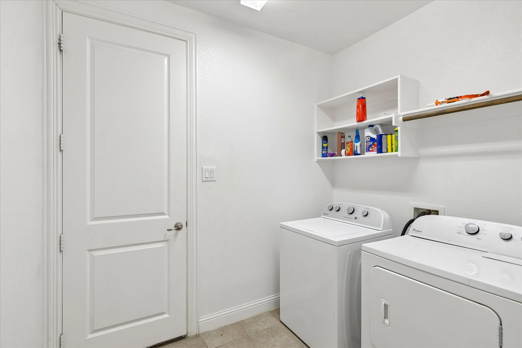 Dedicated laundry area featuring tile flooring, built-in shelving, and a wall-mounted hanging rod