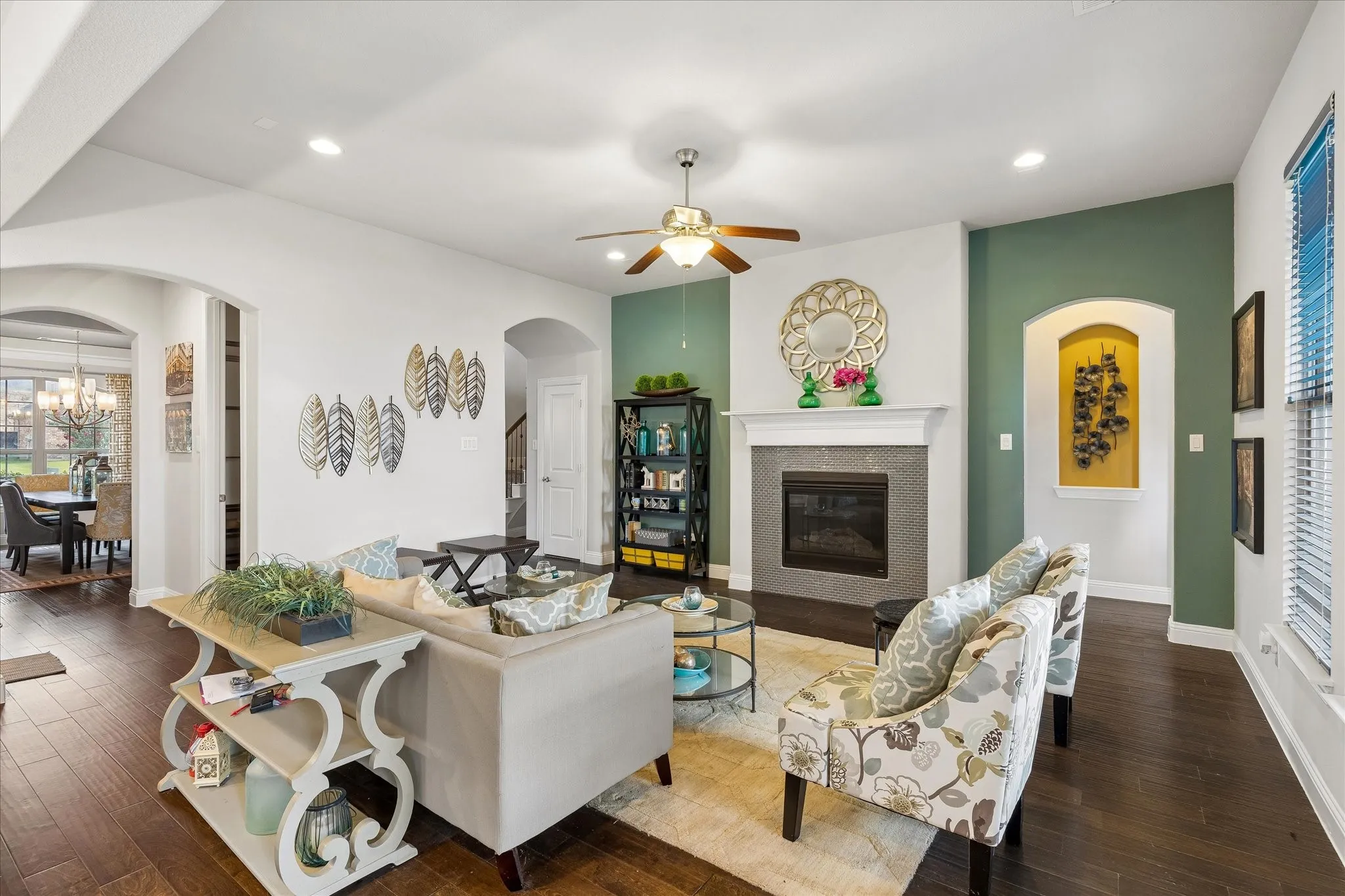Living area featuring wood-finish flooring, a contemporary fireplace with a tiled surround and white mantel, and a ceiling fan with integrated lighting