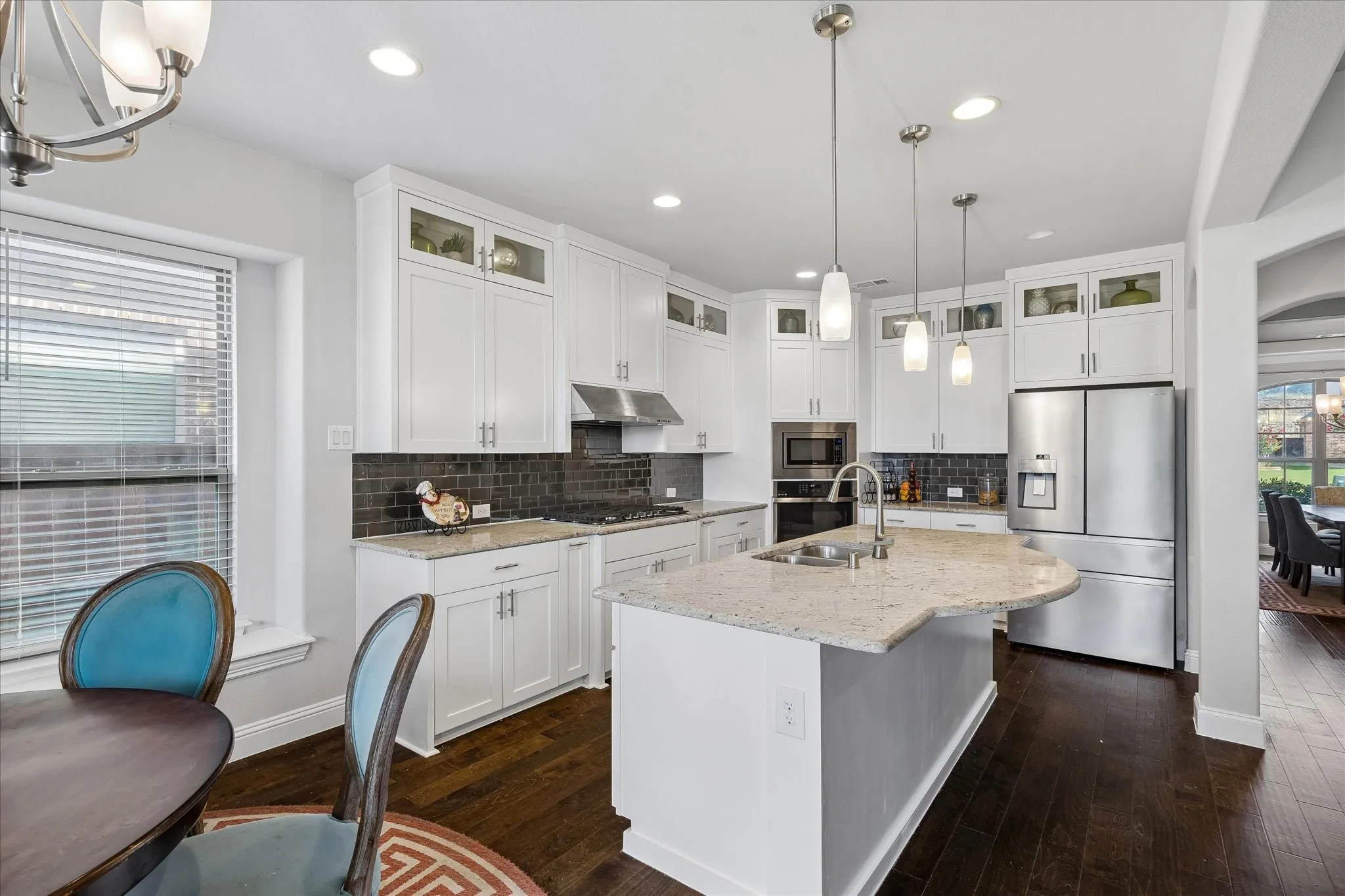 Gourmet kitchen featuring white cabinetry, stainless steel appliances, dark subway tile backsplash, light speckled countertops, and a central island with pendant lighting