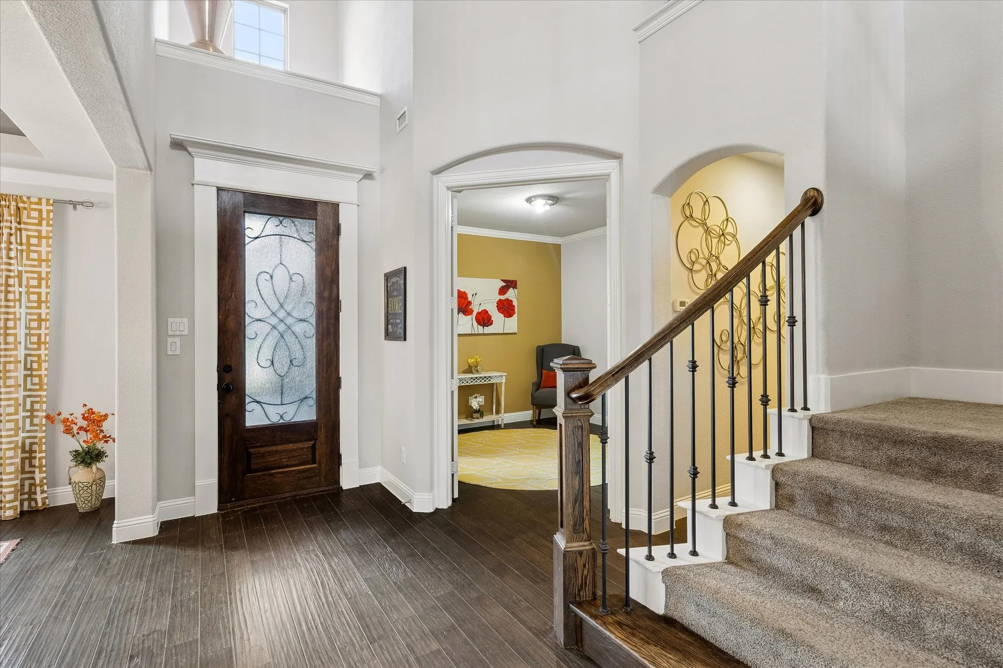 Foyer featuring dark wood-finish flooring, a decorative glass front door, a carpeted staircase with an iron spindle railing, and an arched entryway