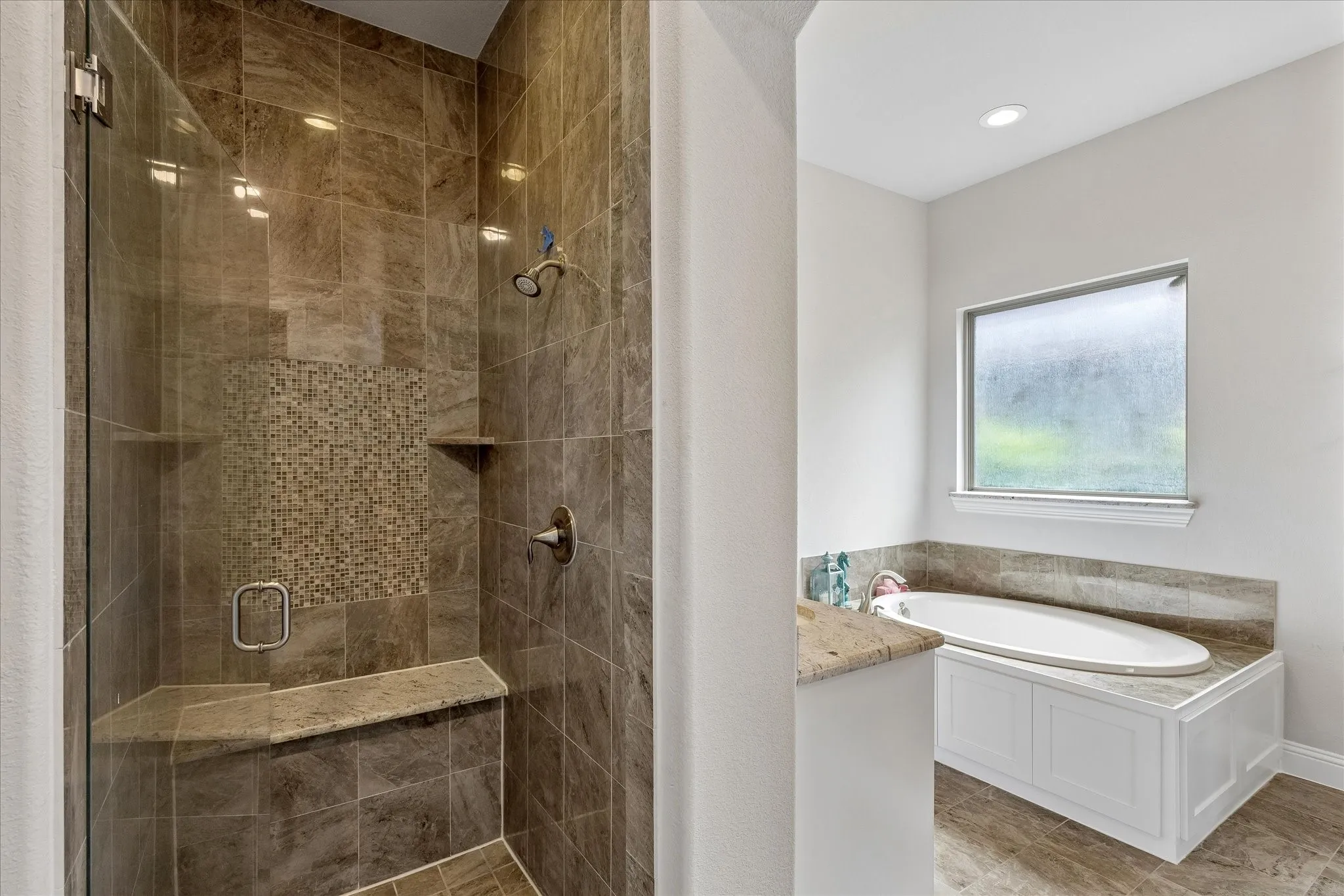 Walk-in shower with full glass enclosure, tiled walls, mosaic tile accent, built-in bench, and corner shelf