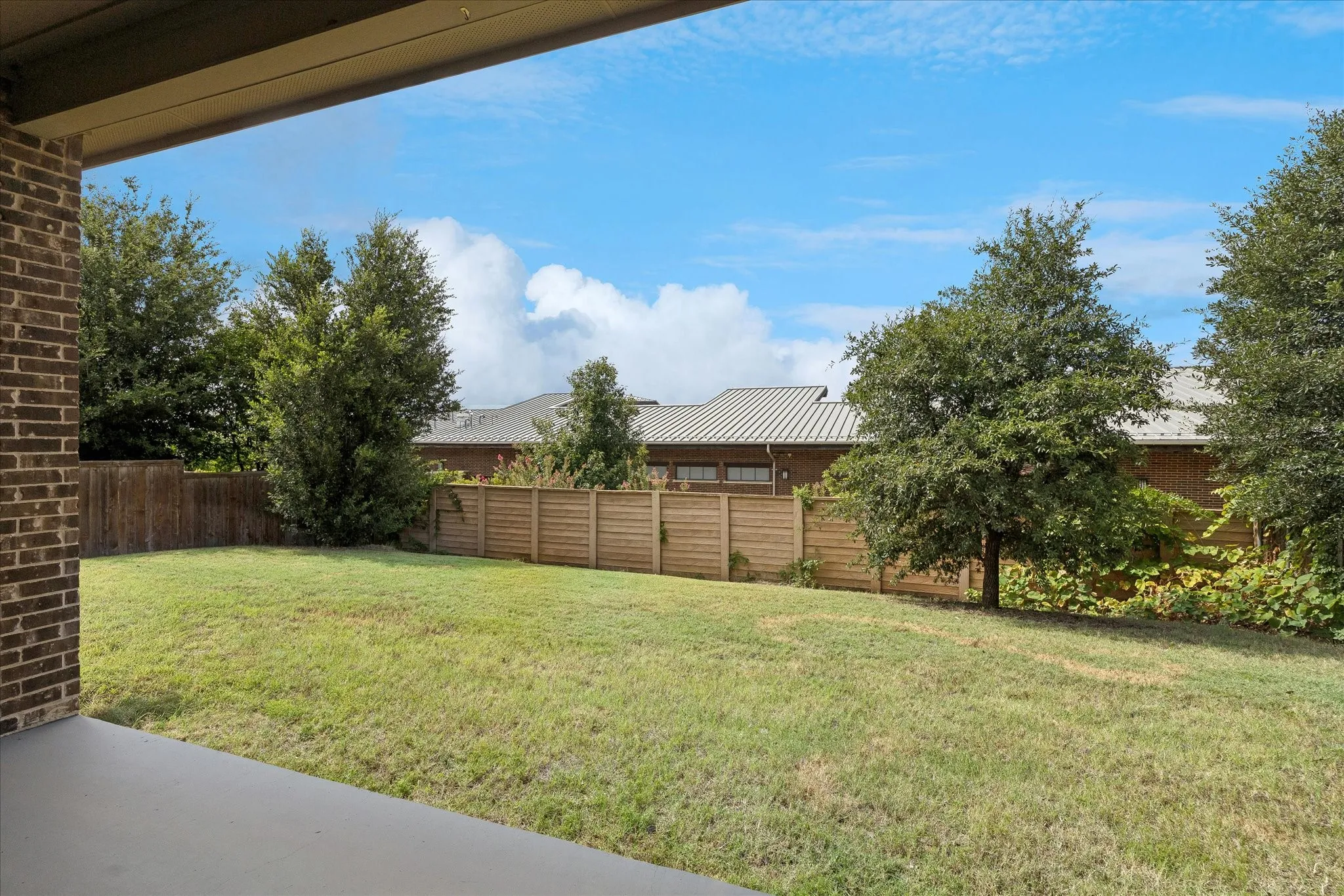 Spacious backyard featuring a large grass lawn, privacy fencing, and mature perimeter trees